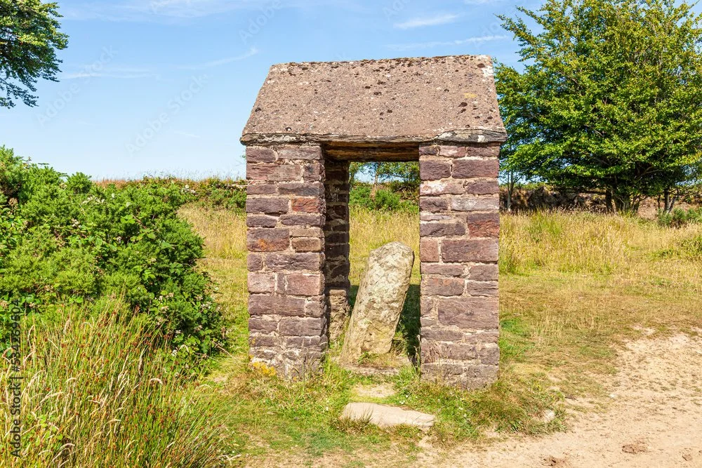 A small brick shelter in a grassy field with trees in the background, containing a large standing stone.