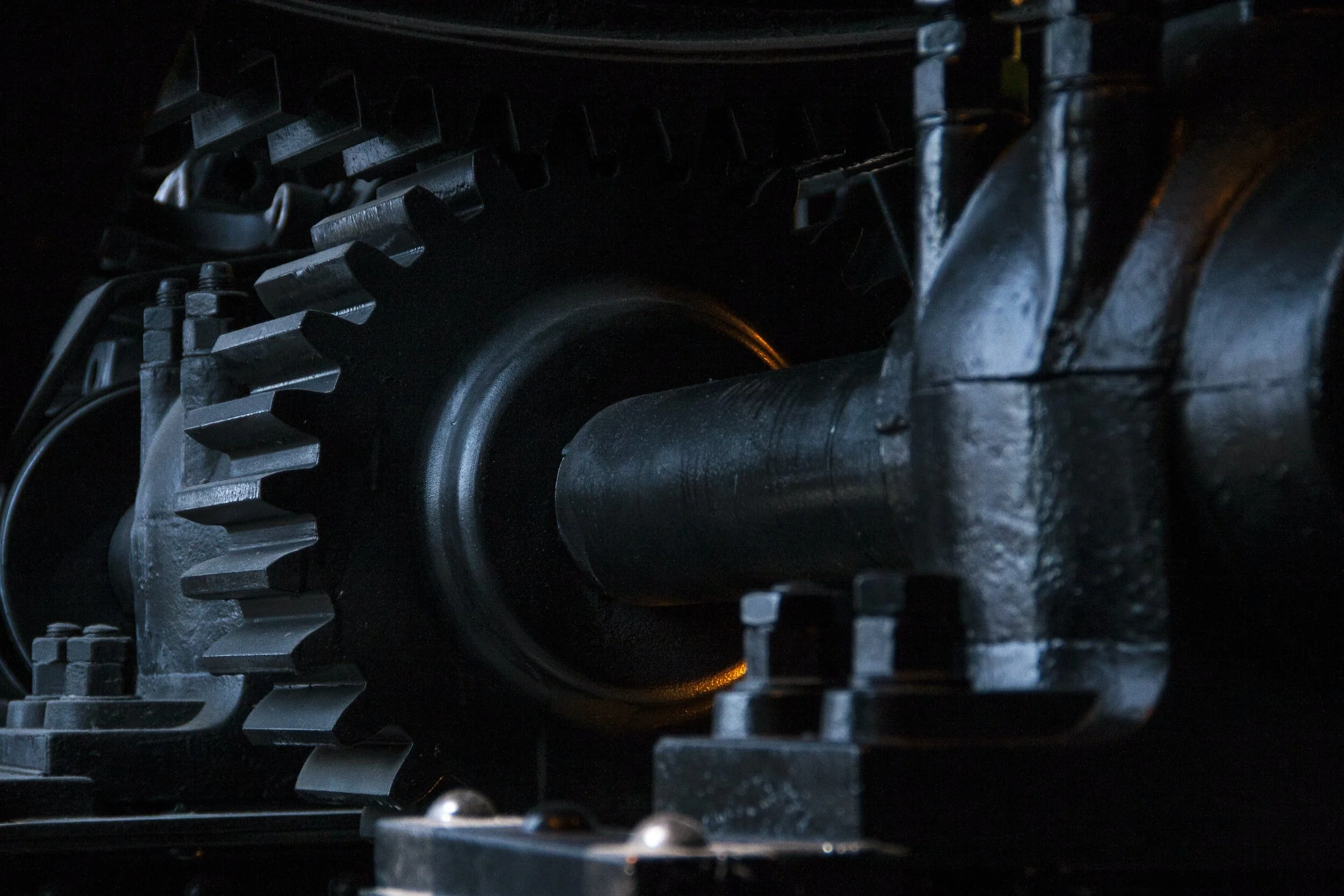 Close-up of a large metal gear and shaft assembly, part of heavy machinery or industrial equipment, in a dark setting.
