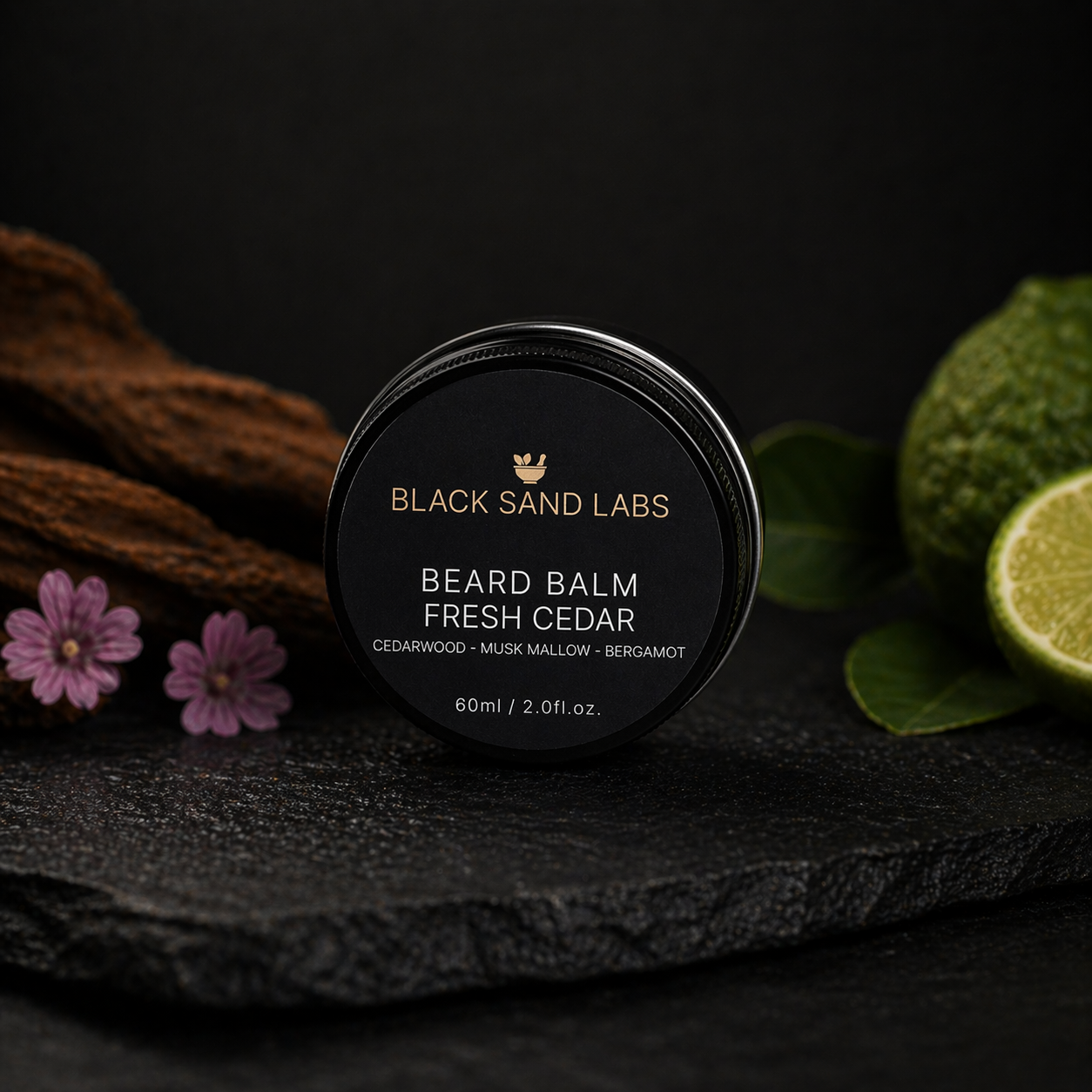 Black Sand Labs beard balm container labeled 'Fresh Cedar' with cedarwood, musk mallow, and bergamot ingredients, placed on a dark textured surface with cinnamon sticks, pink flowers, and halved lime in the background.