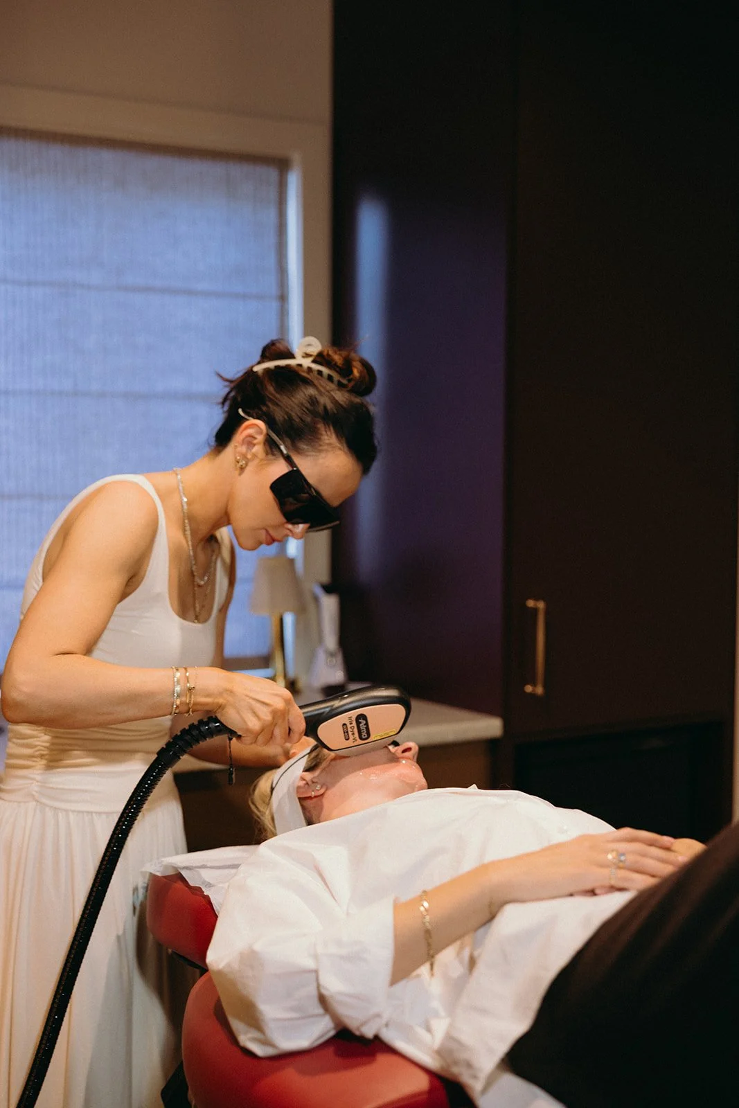 Beauty professional performing a facial treatment with a handheld device on a reclining client wearing protective eyewear