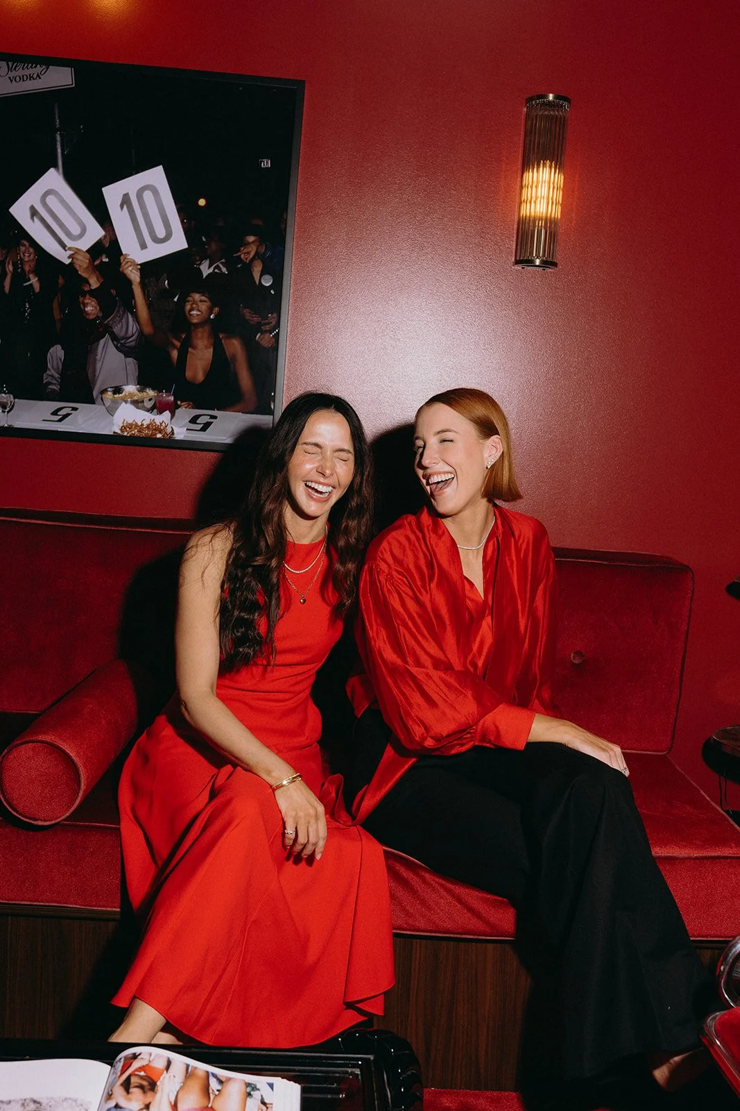 Two members of the Bellix team laughing together on a red velvet banquette in the New Farm clinic lounge