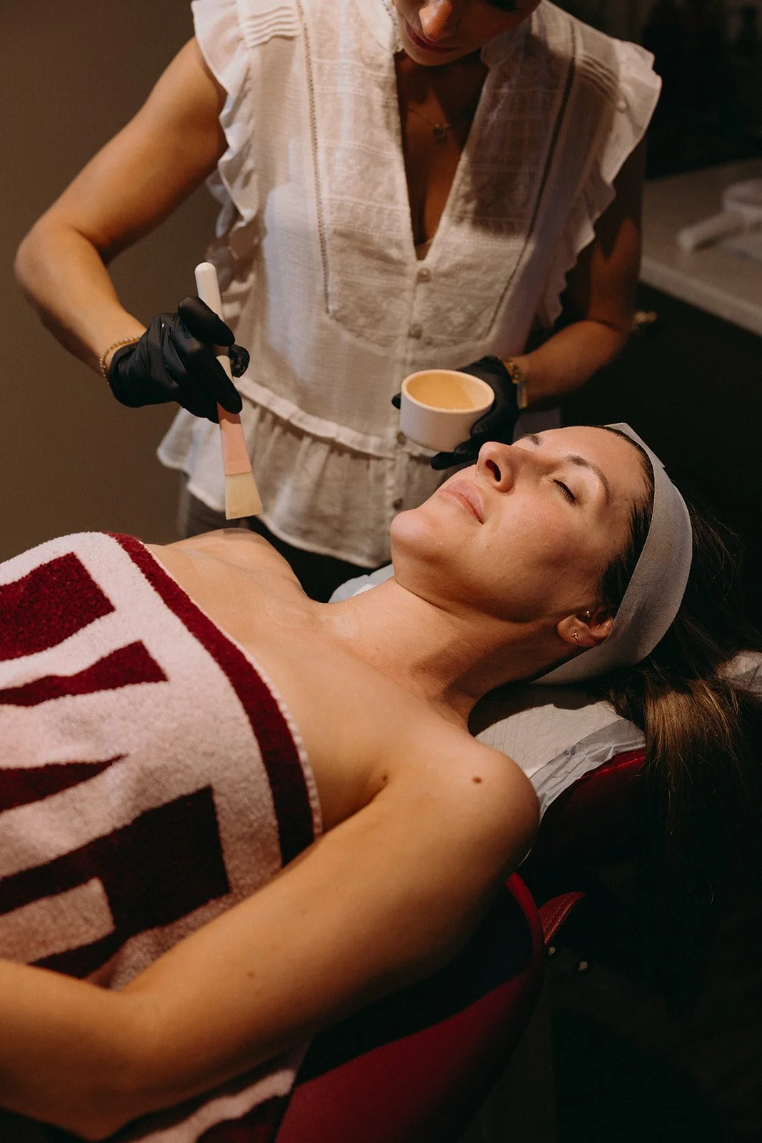 Esthetician applying a facial treatment with a brush to a relaxed woman at a spa