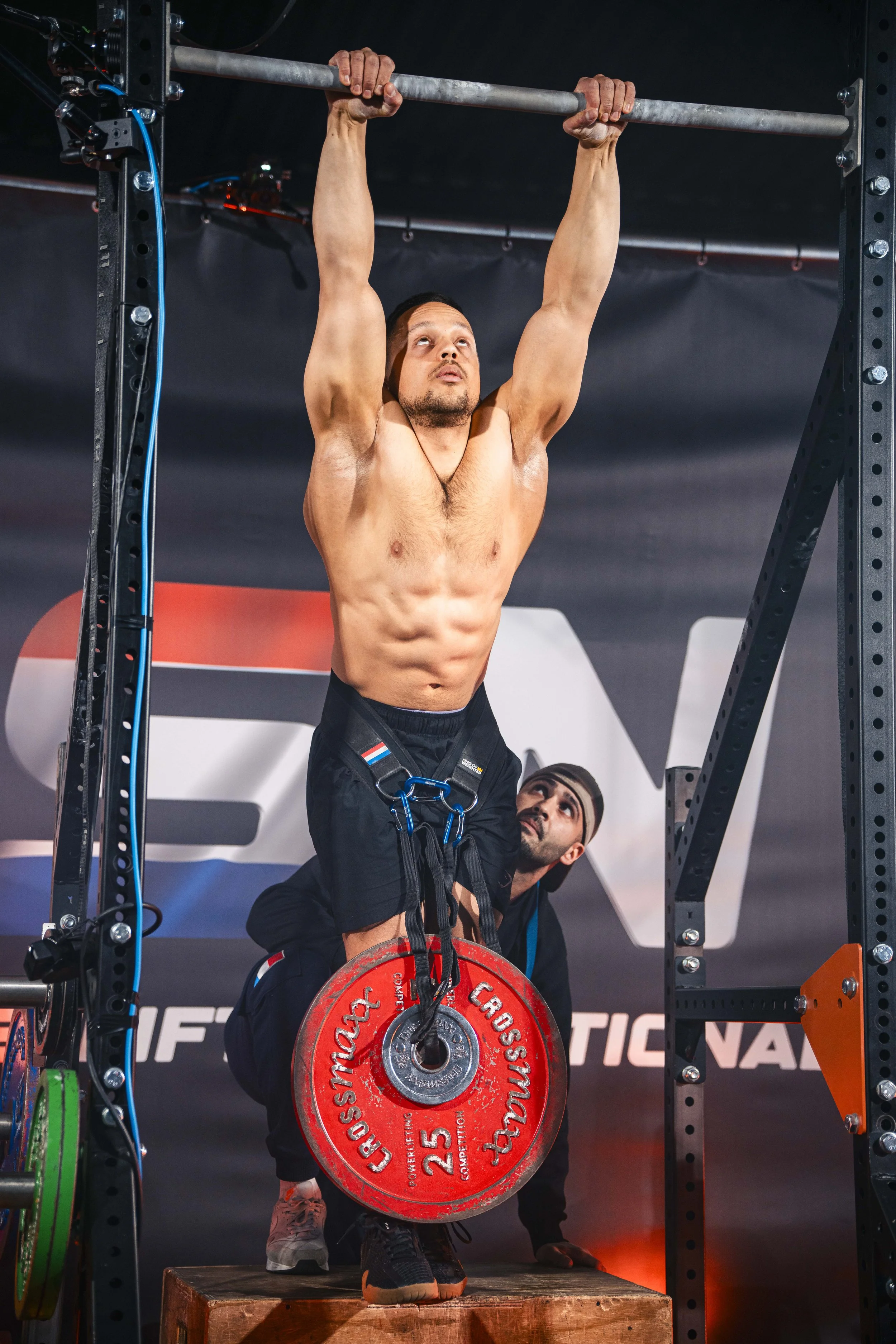 Man dat een gewicht hecht aan een dip belt, terwijl hij op een platform staat en wacht op het startsignaal tijdens een fitnesscompetitie.