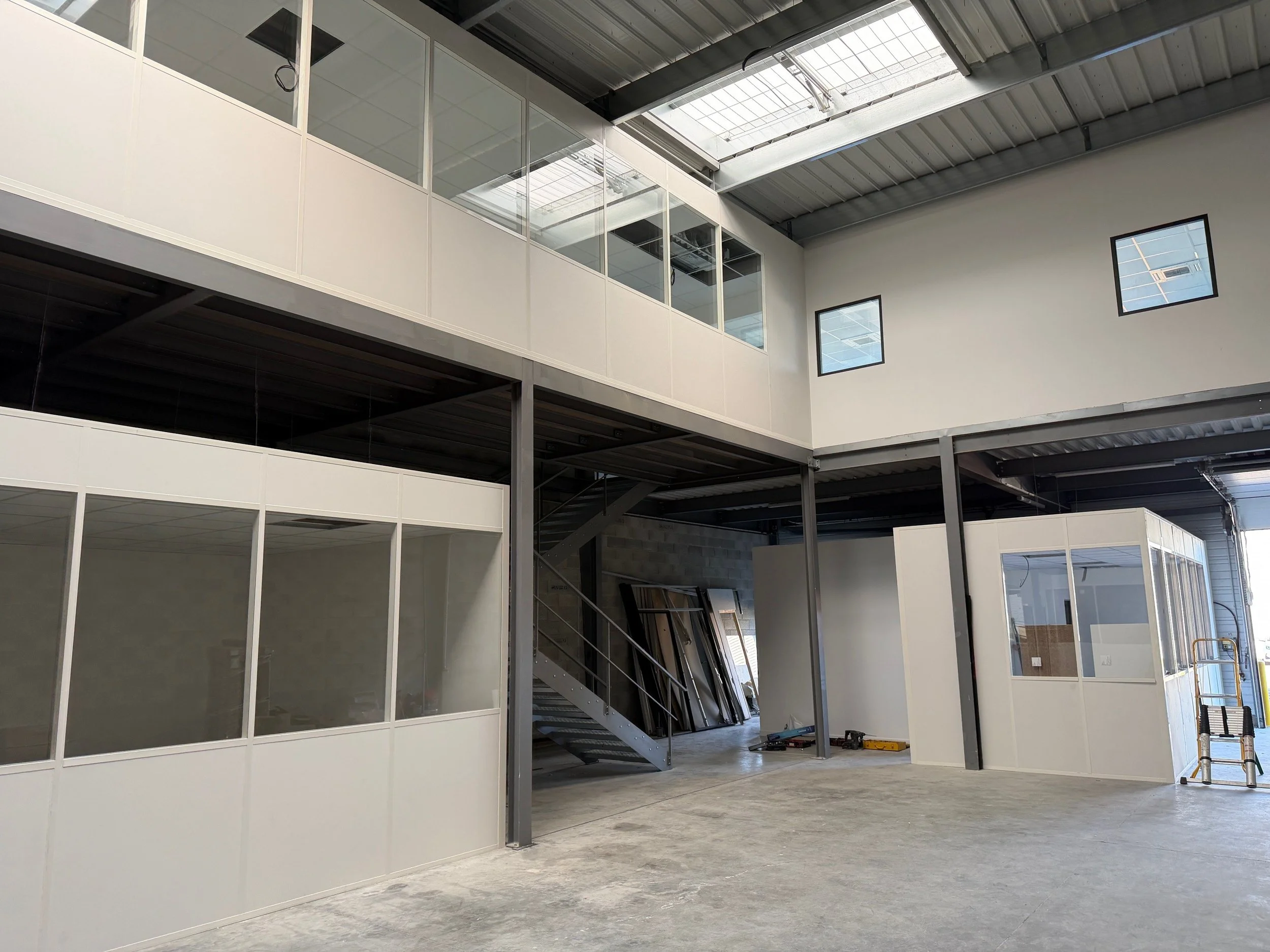 Intérieur d'un bâtiment industriel ou local d'activité avec une plateforme métallique, des cloisons vitrées sur allège, un escalier en métal, des bureaux et laboratoires en cloisons amovibles avec faux-plafond 600x600.