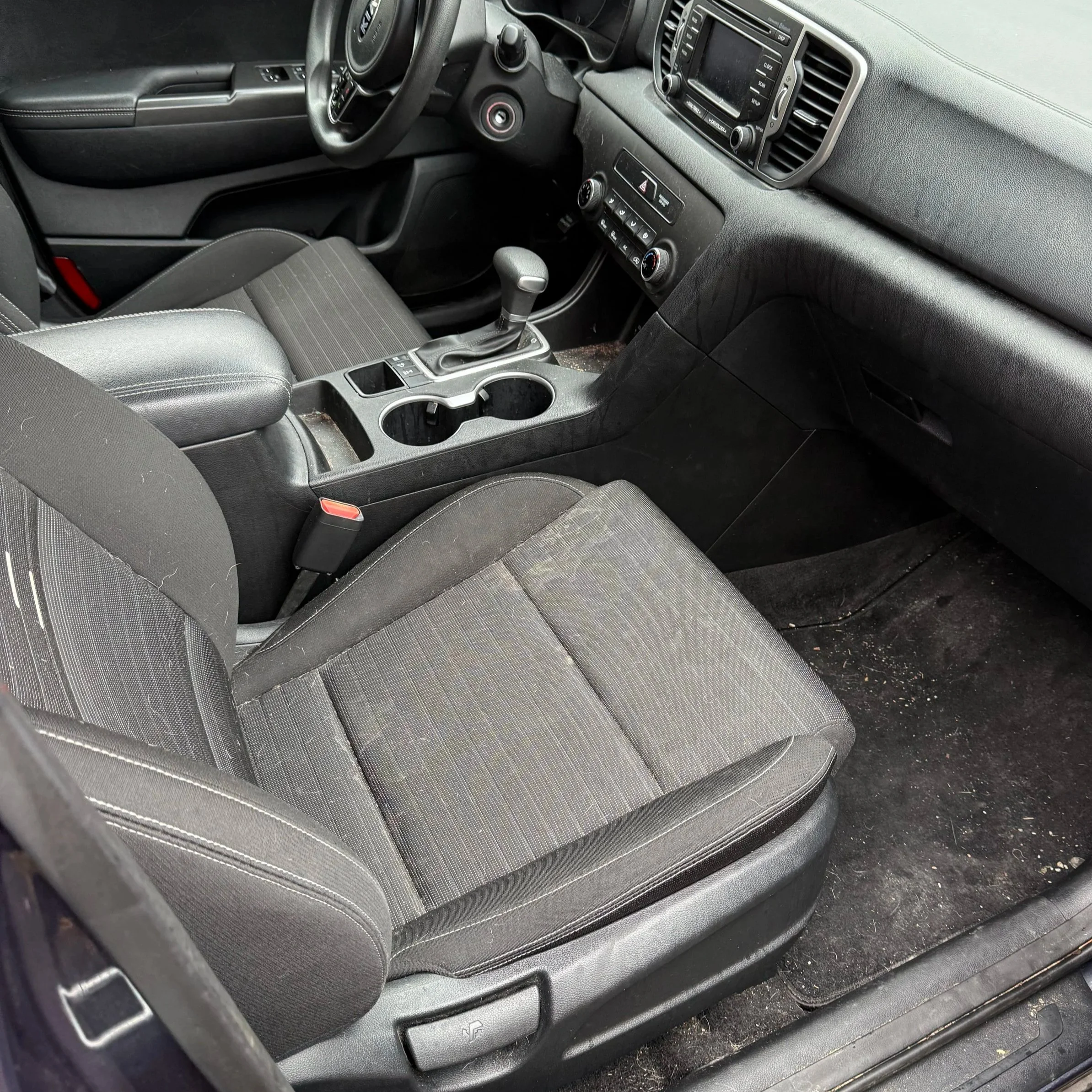 The interior of a vehicle showing the front passenger seat, center console with cup holders, gear shifter, and dashboard with controls and a screen.