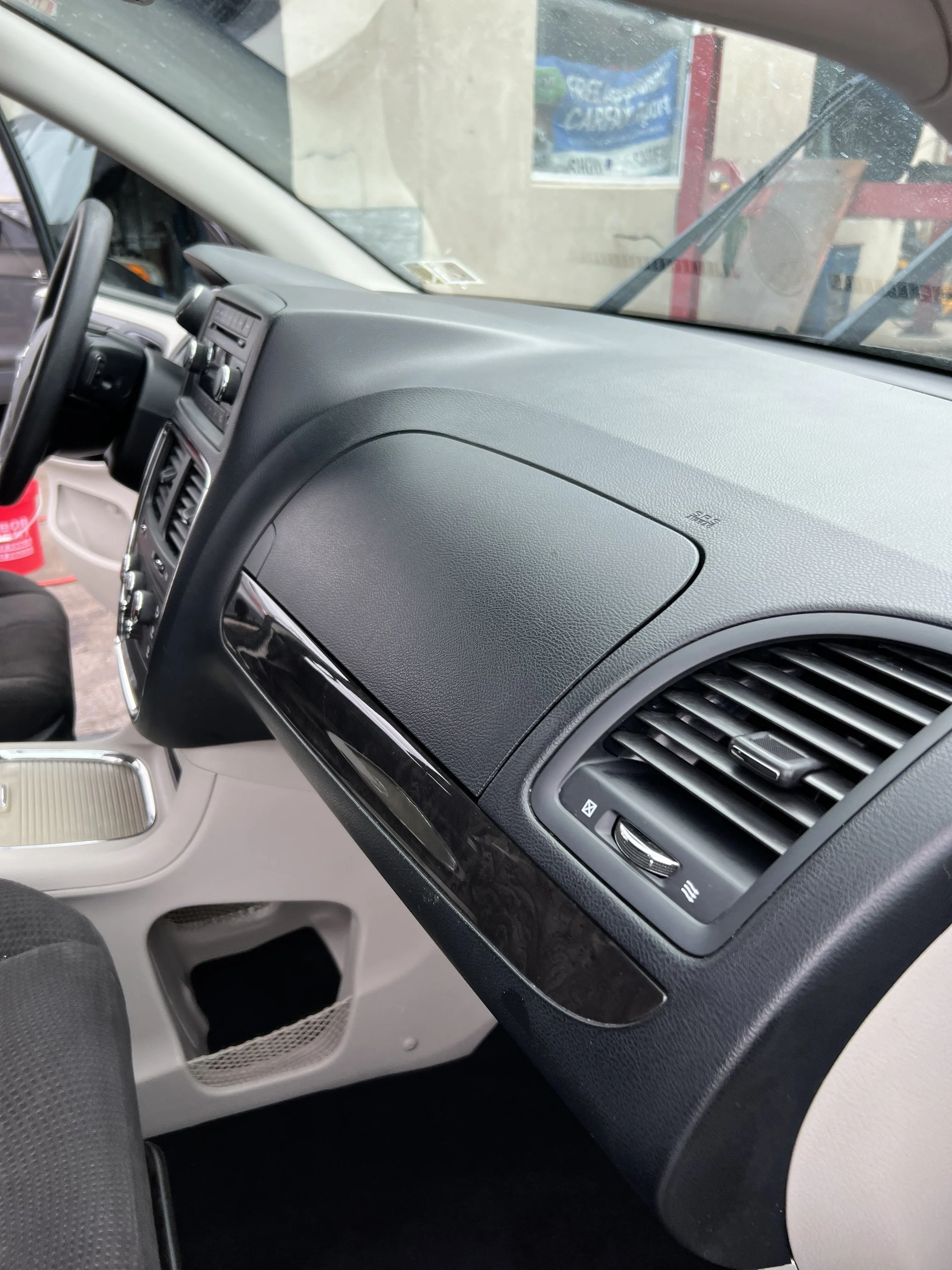 View of car interior showing dashboard with air vents, control panel, and steering wheel on the left.