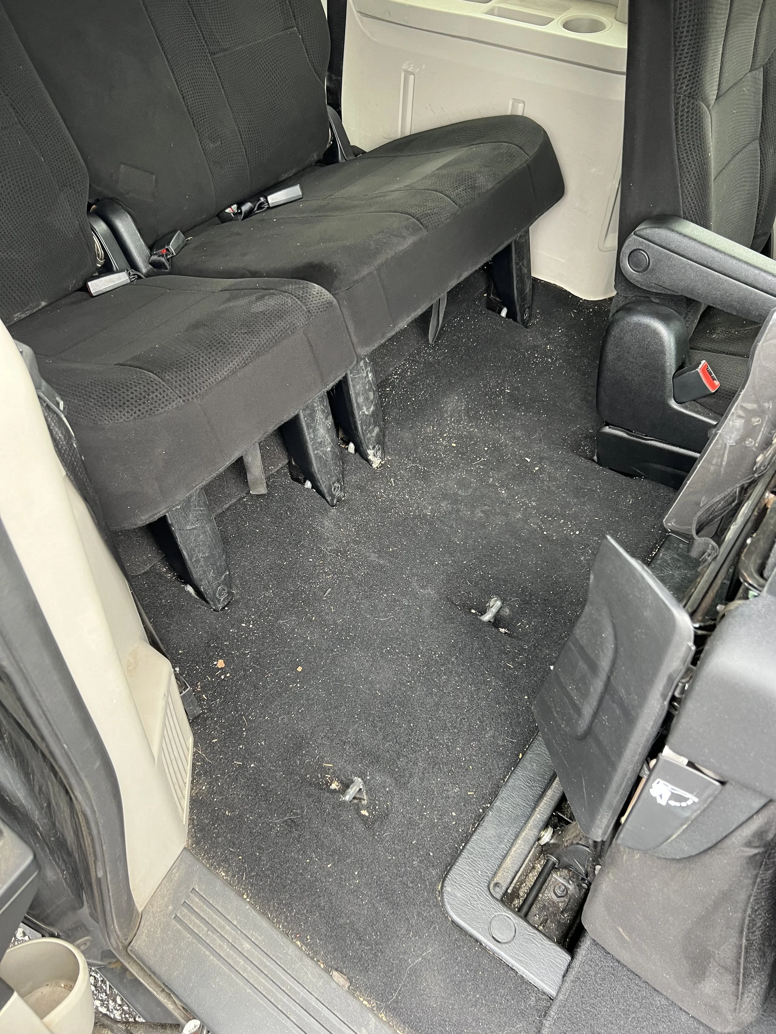 Photo of the interior of a vehicle showing the back seats and floor, which is dirty and has some debris.