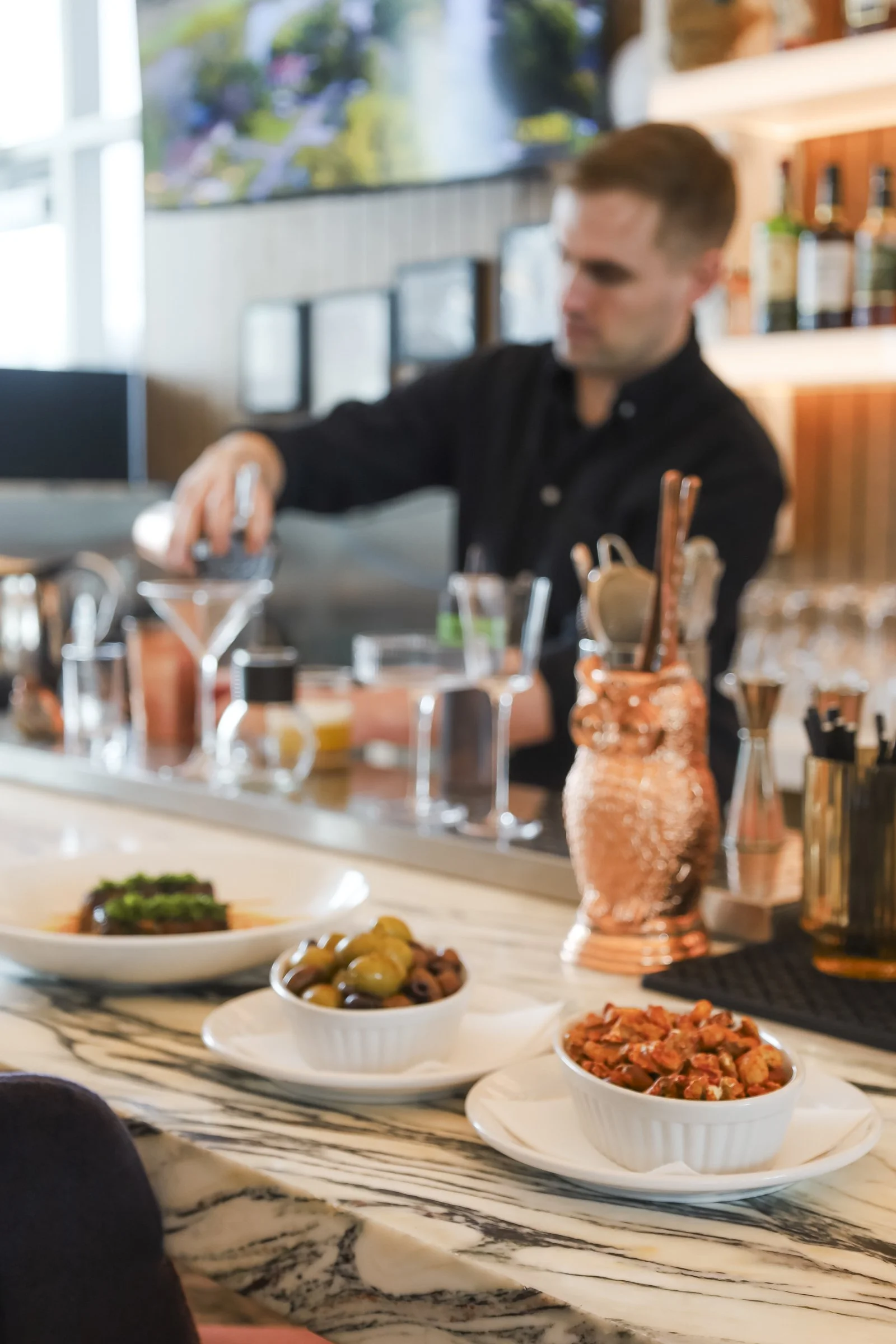 Bartender crafting cocktails behind the bar with small plates and olives at an Old Montreal pub, highlighting the vibrant Montreal bar atmosphere of a British pub Montreal in the heart of Old Montreal.