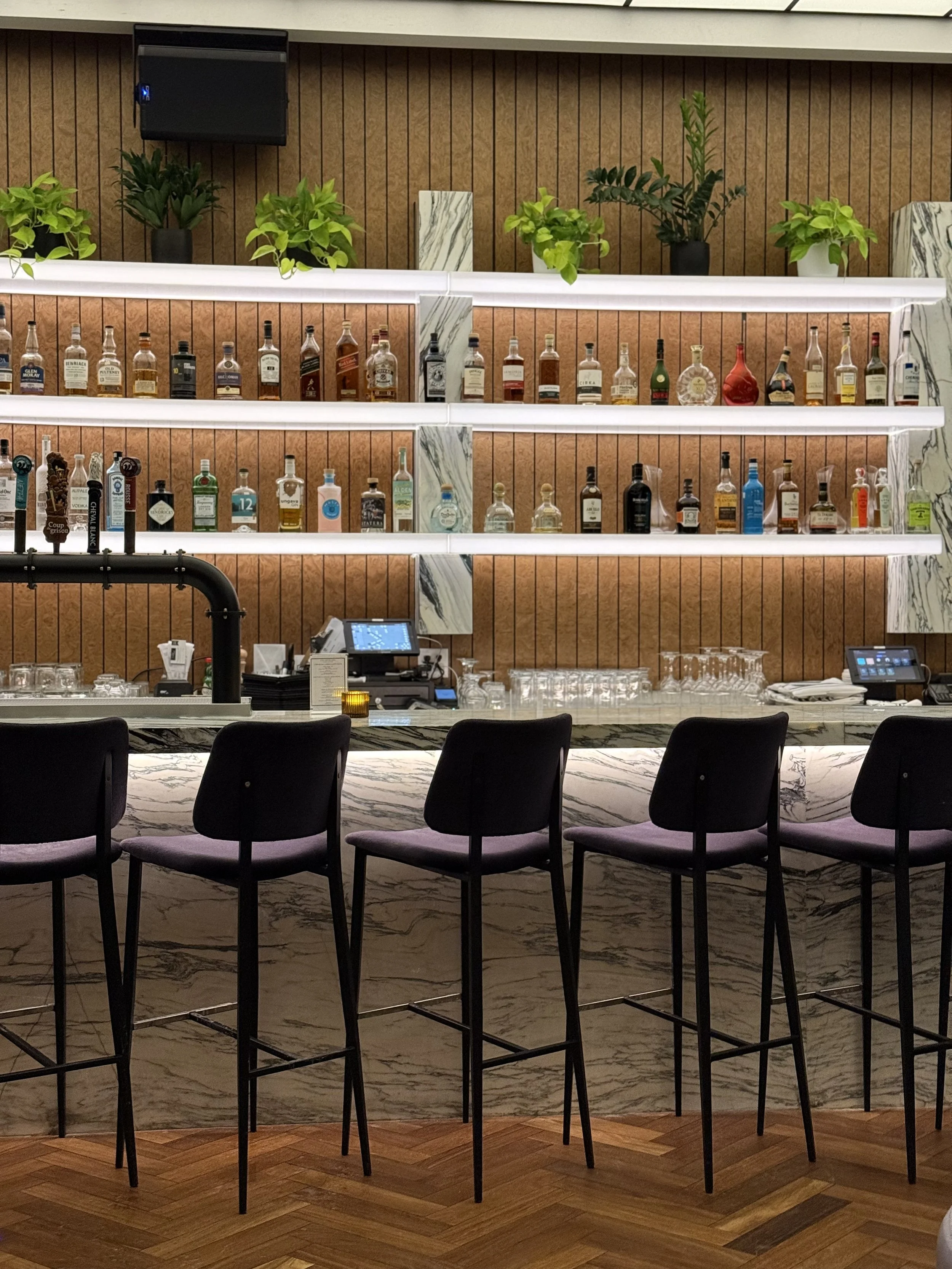 Modern marble bar with curated spirits and high stools at a British pub Montreal in Old Montreal, showcasing the refined yet welcoming Montreal bar atmosphere of a vibrant Old Montreal pub.