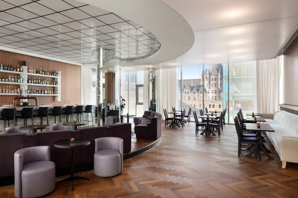 Bright dining room with floor-to-ceiling windows overlooking Castle Viger, featuring a central bar and elegant seating at a British pub Montreal in Old Montreal, offering a refined Montreal restaurant Old Montreal experience with a unique castle view