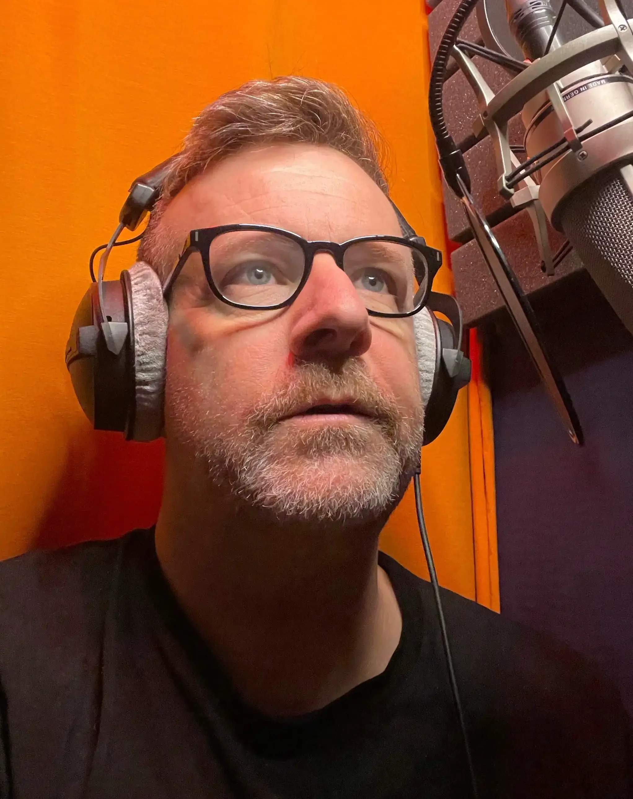 Man wearing glasses and headphones in recording booth