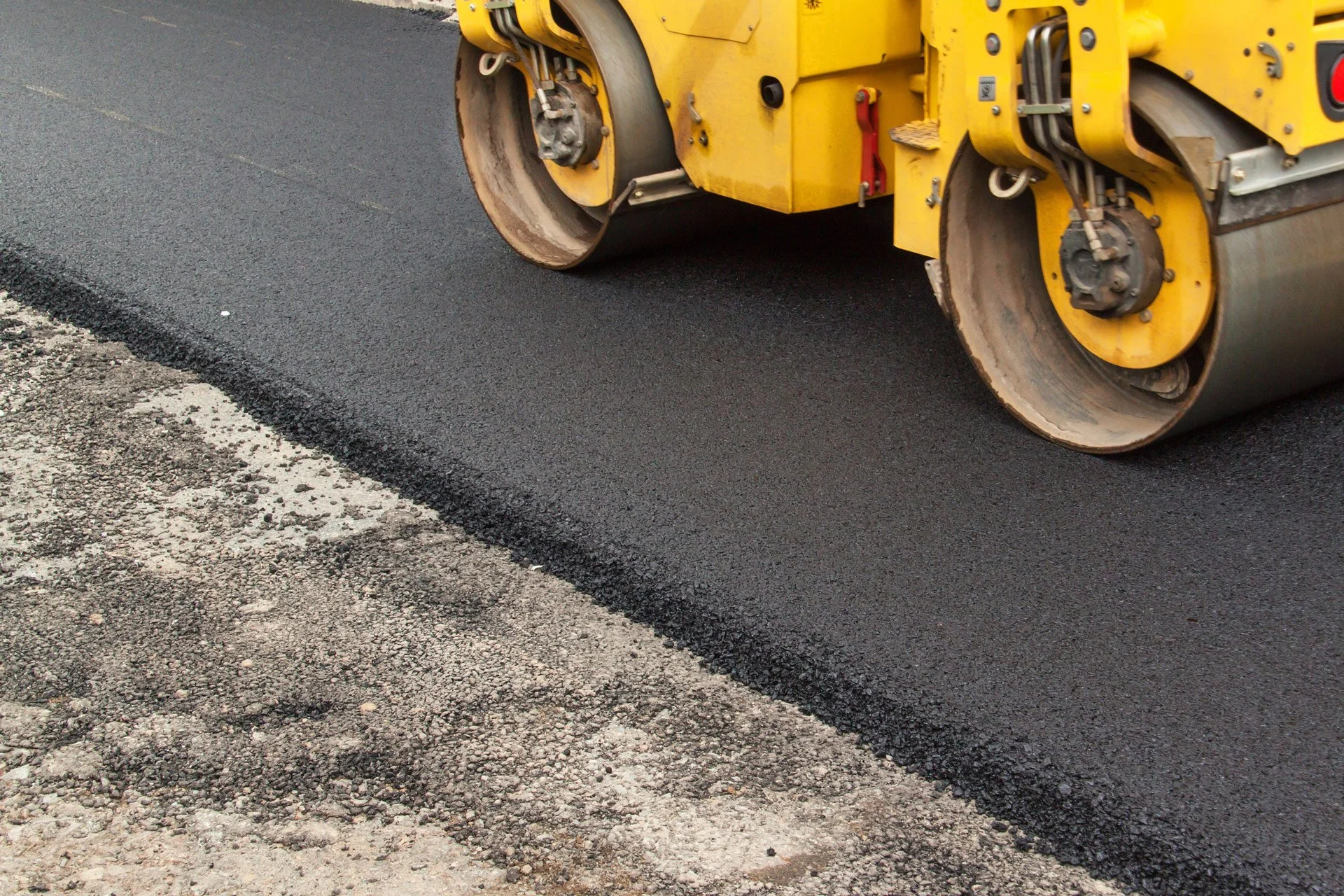 A yellow road roller compacting fresh asphalt on a road surface