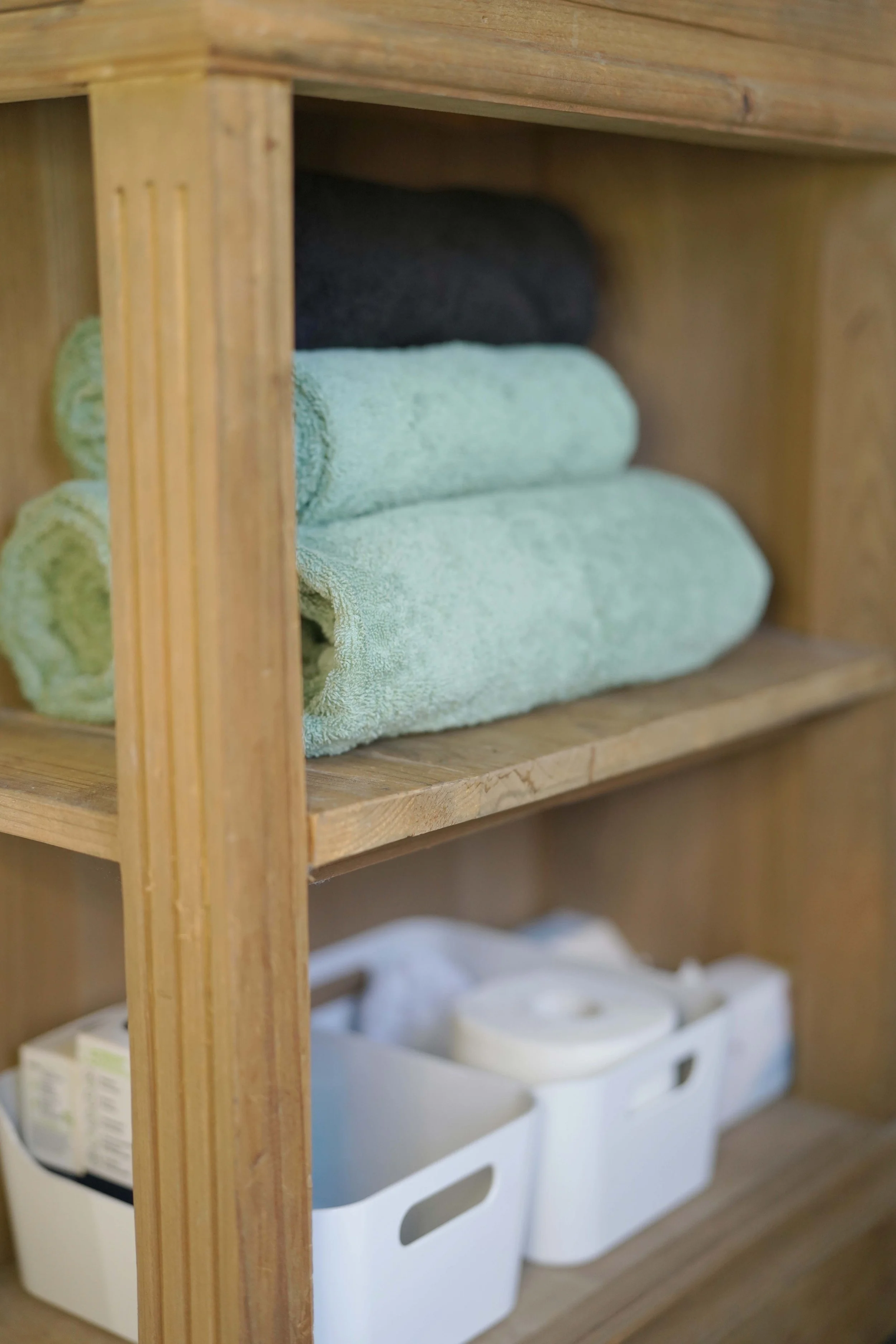 Badezimmerregal mit gefalteten Handtüchern in Grau und Grün und weissen Aufbewahrungsboxen mit Toilettenartikeln.