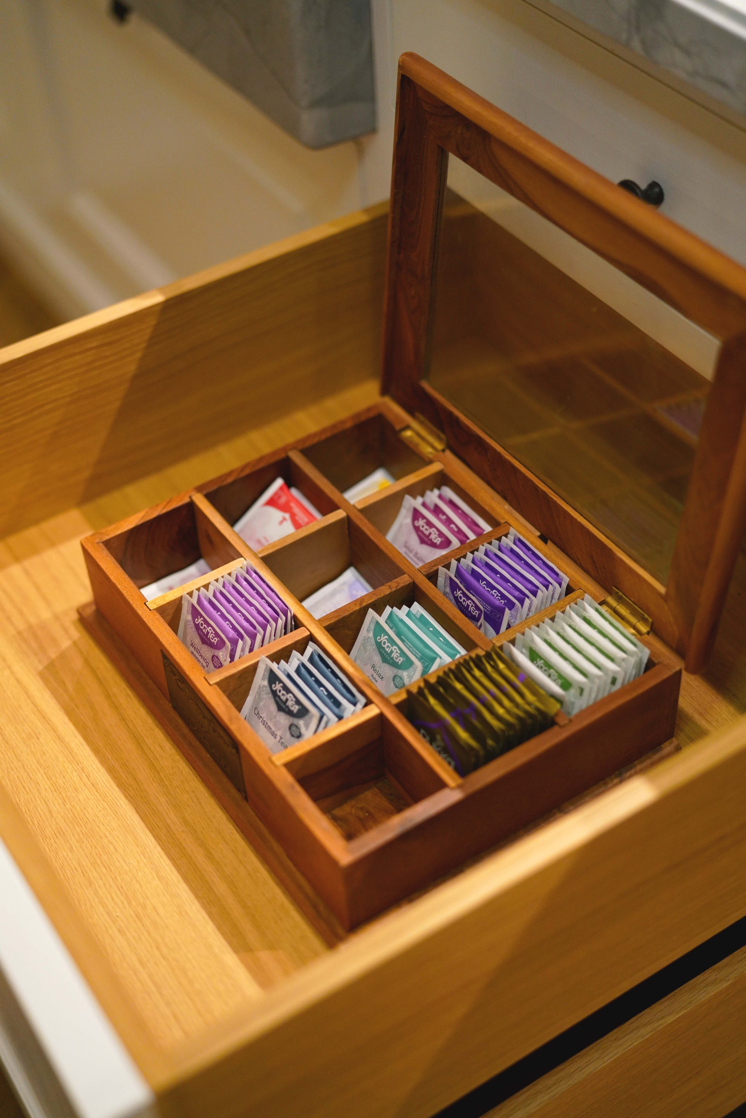 Ein Holzkästchen mit verschiedenen Teesorten in Einzelverpackungen, offen auf einem Holztisch