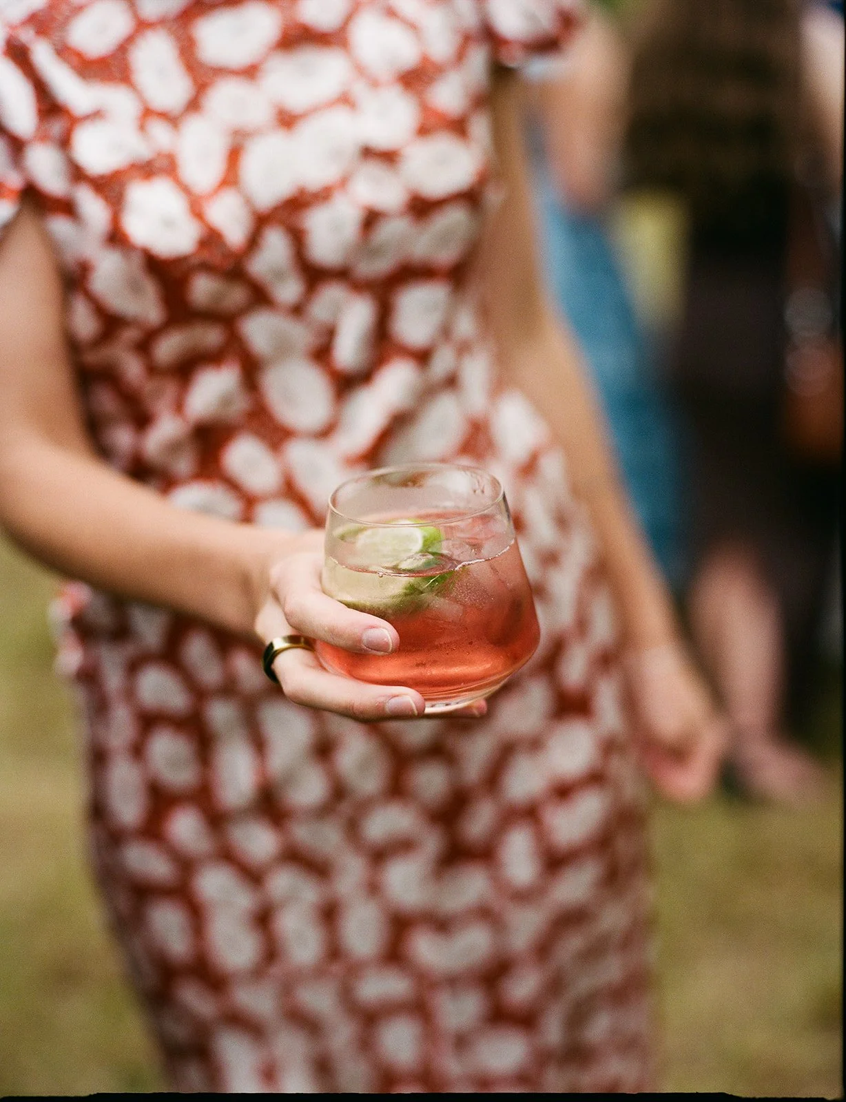 Wedding guest holding a custom handcrafted cocktail from Eido Bar Company, smiling during an outdoor wedding reception.
