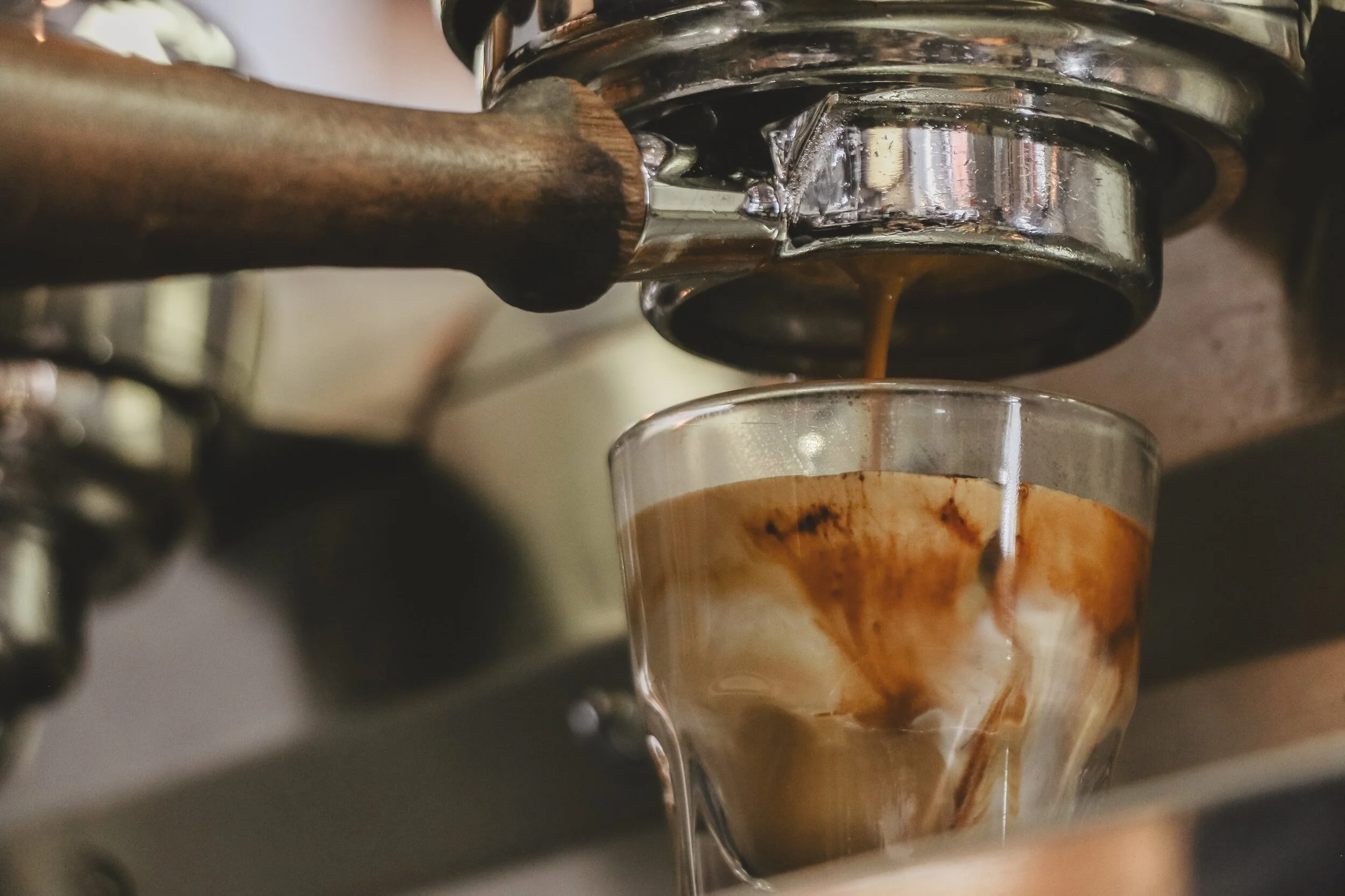 Espresso being poured from a portafilter into a clear glass on a coffee machine.