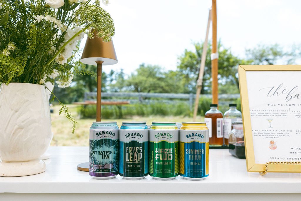 Sebago Brewing Company beer cans displayed on a bar top, neatly arranged for guests at an event.