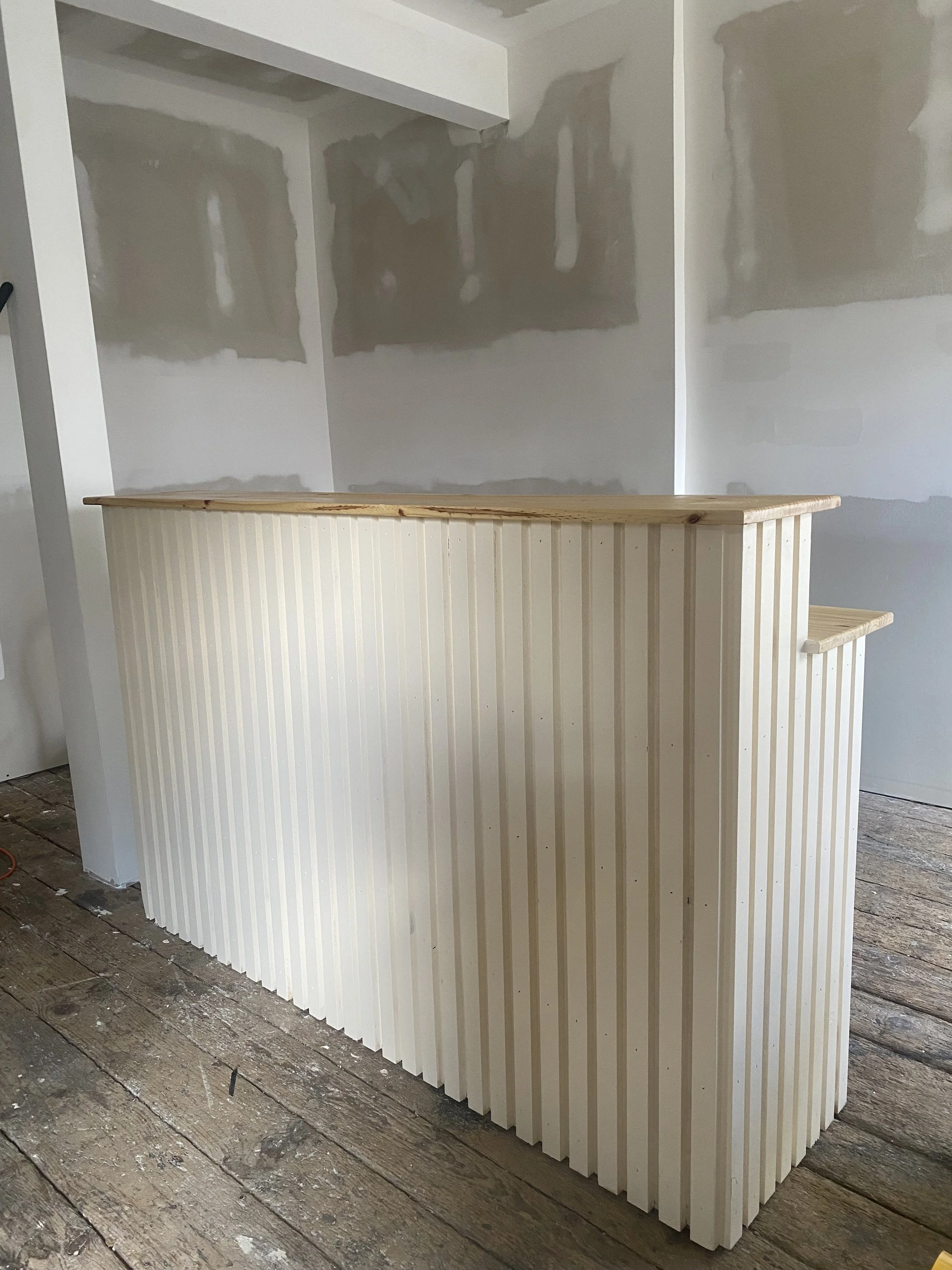 Wine bottles on a wooden box with more bottles in containers, glasses and people in the background.