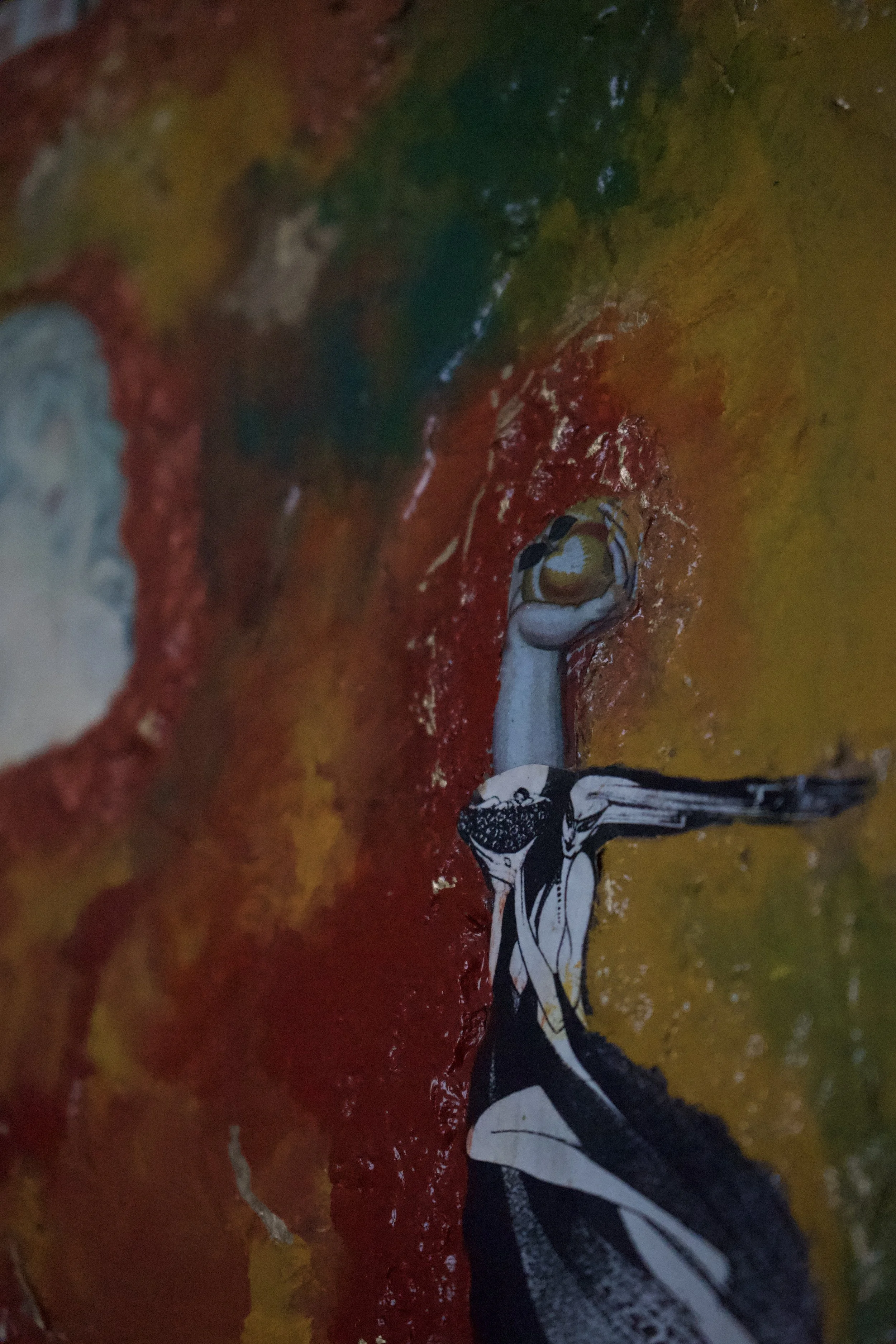 Close-up view of graffiti art featuring a stylized human figure with an elongated neck and a black and white body, against a colorful, textured background of red, yellow, green, and blue paint.