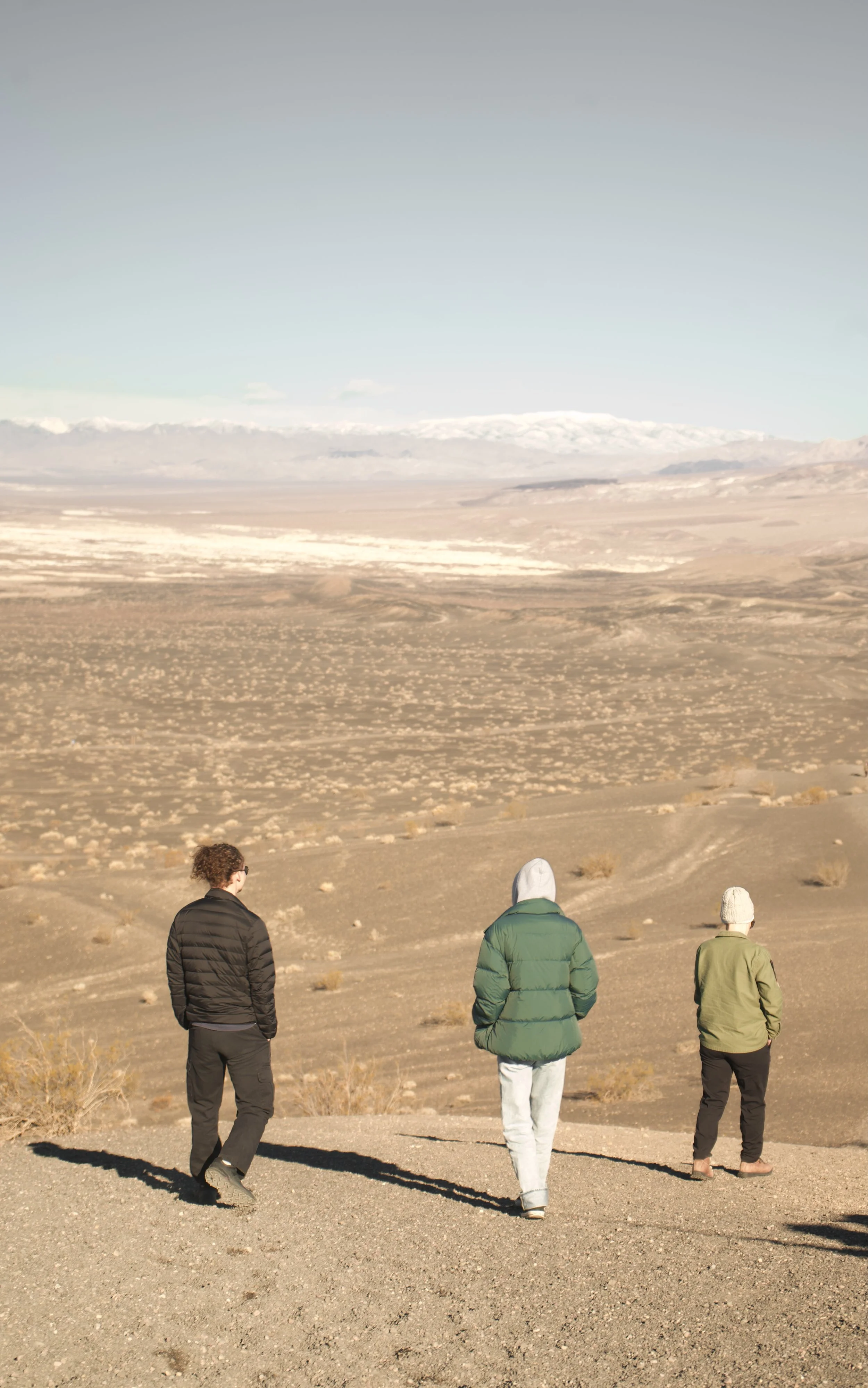 Three people walking in a desert landscape with mountains in the distance under a clear sky.