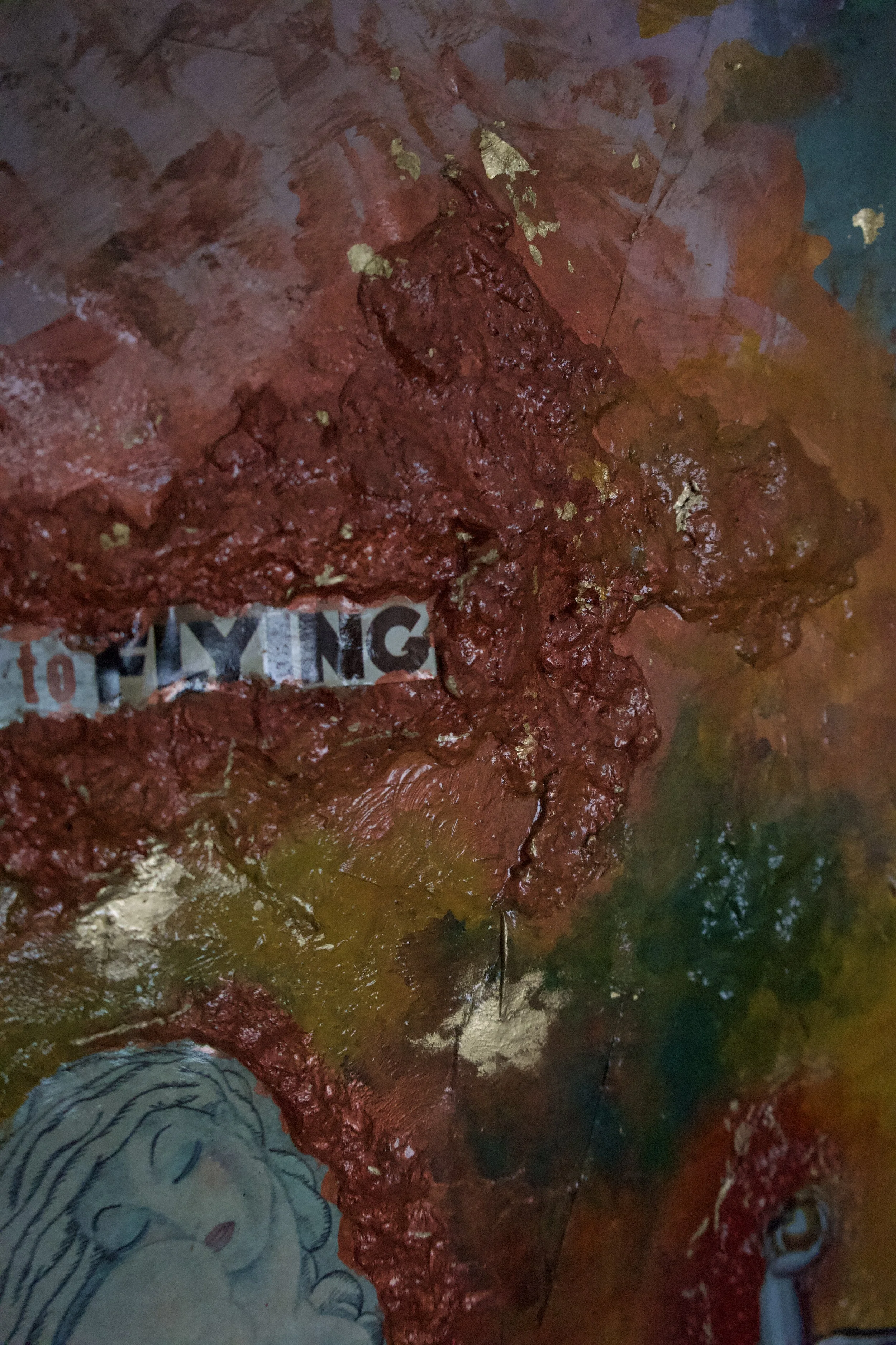 Close-up of a colorful abstract painting with textured red, green, yellow, and blue paint, including a partial drawing of a smiling face in the bottom left corner.