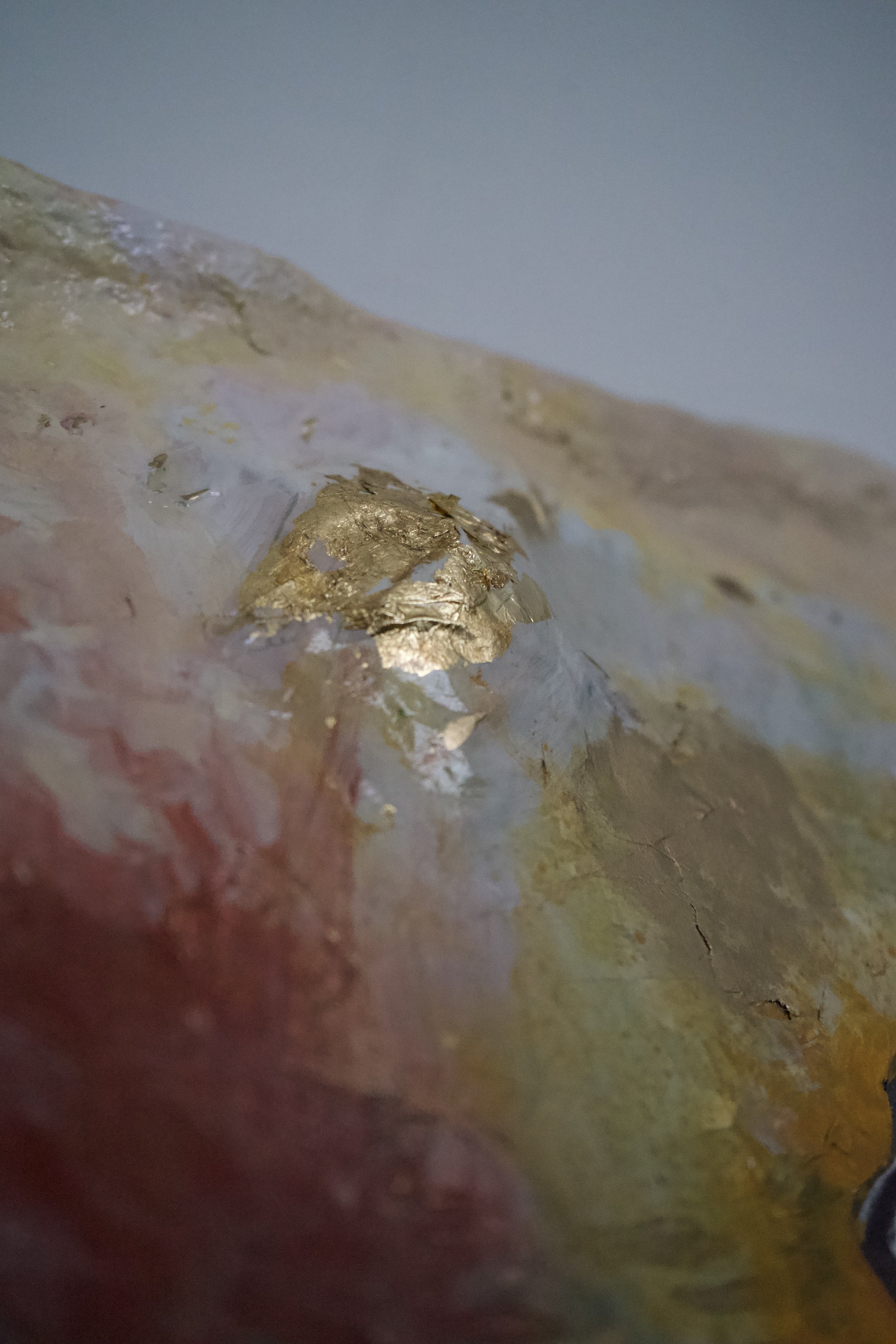 Close-up of a textured, abstract surface with patches of gold and various pastel colors.