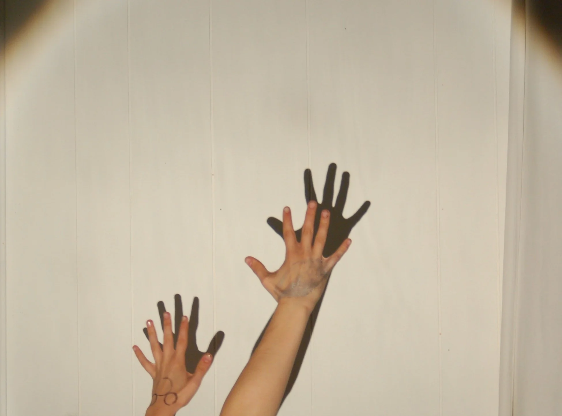 Two hands with painted nails reaching towards a wall, casting shadows that resemble larger, different hands.