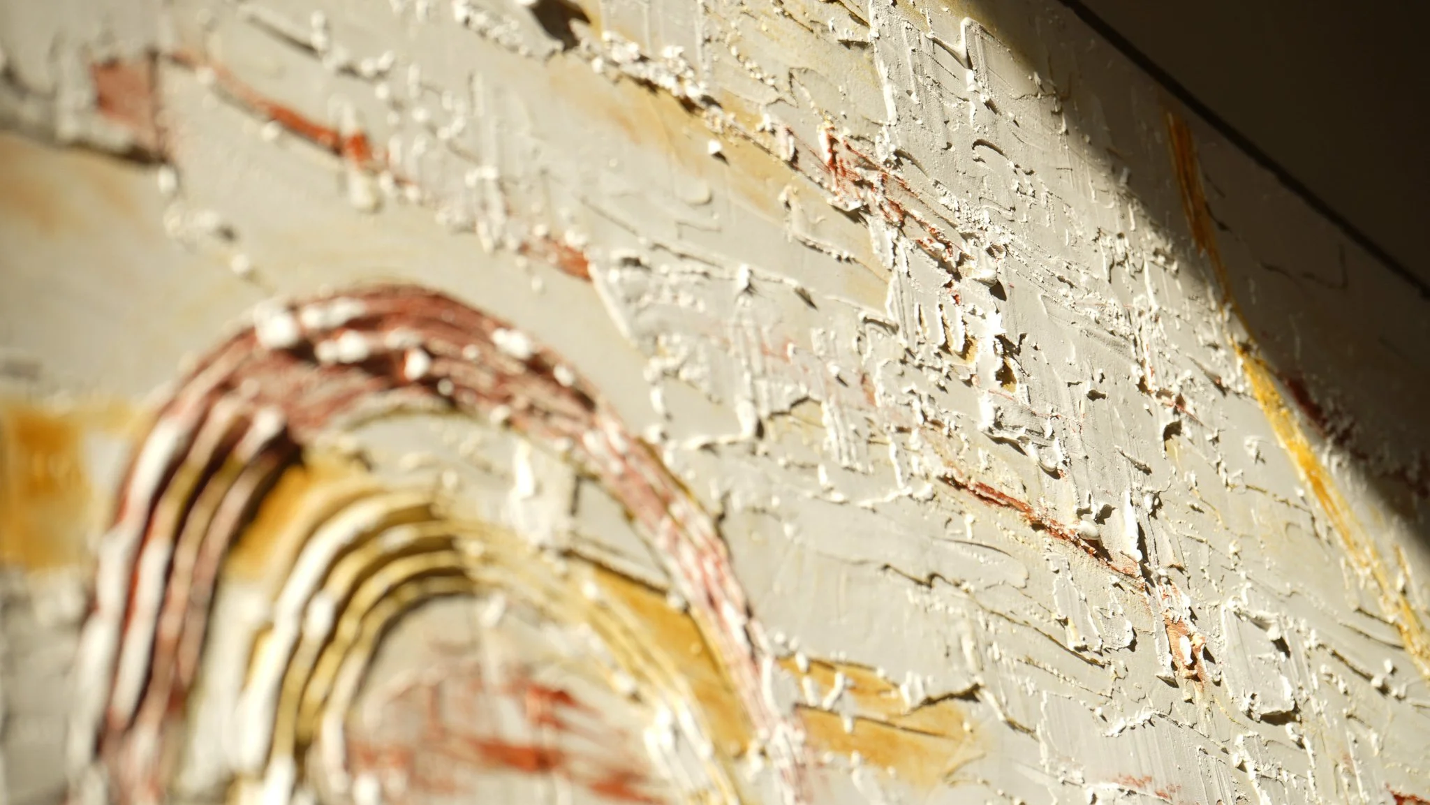 Close-up of a textured, painted wall with abstract patterns in white, gold, and brown colors.