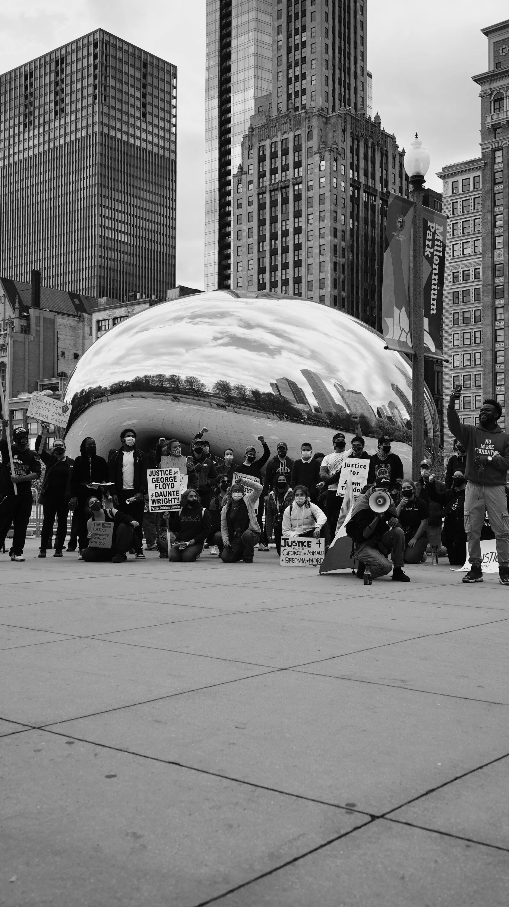 Group of protesters holding signs and raising fists in front of Cloud Gate sculpture in Chicago's Millennium Park.