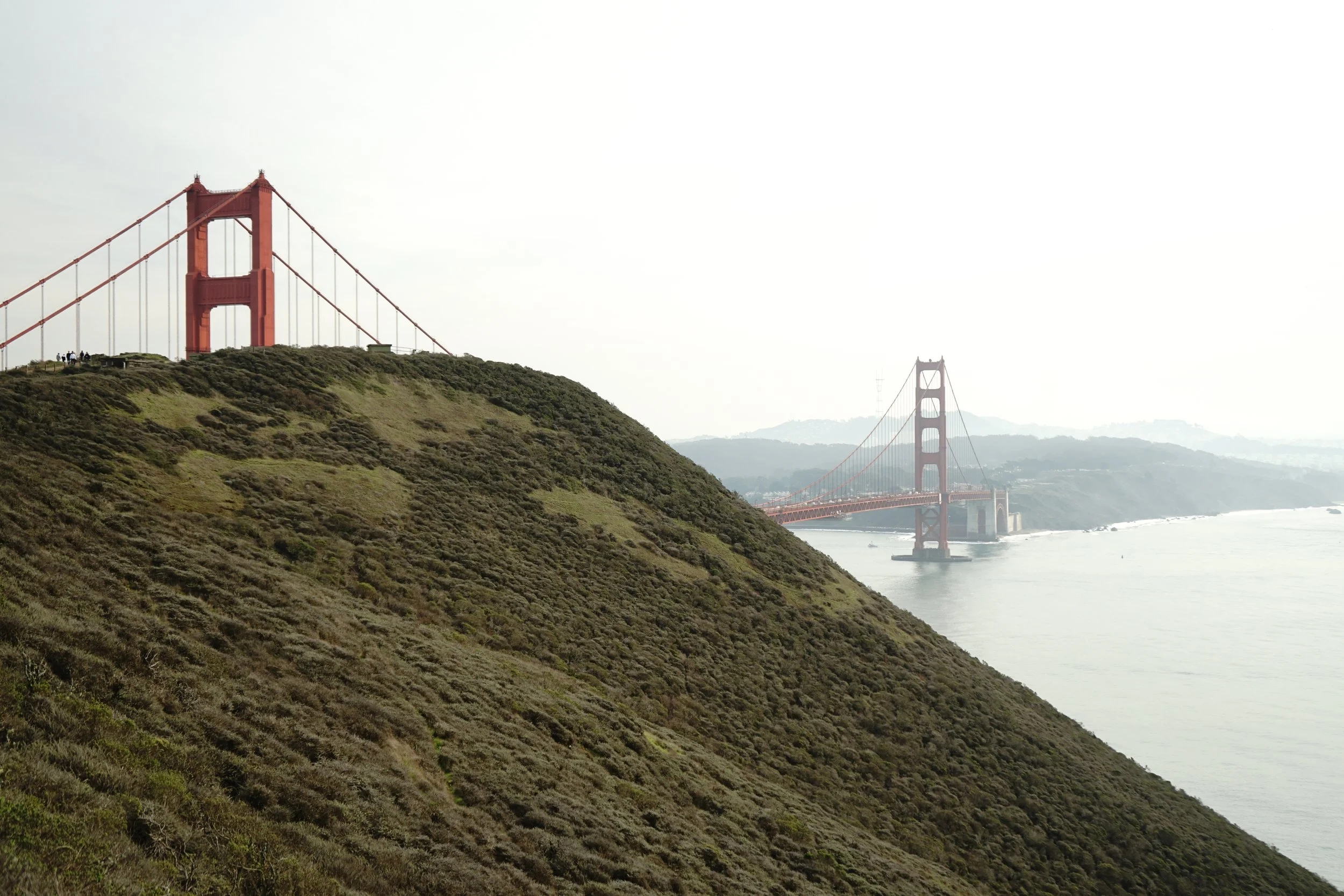 View of the Golden Gate Bridge in San Francisco, partially obscured by a hillside with green vegetation.