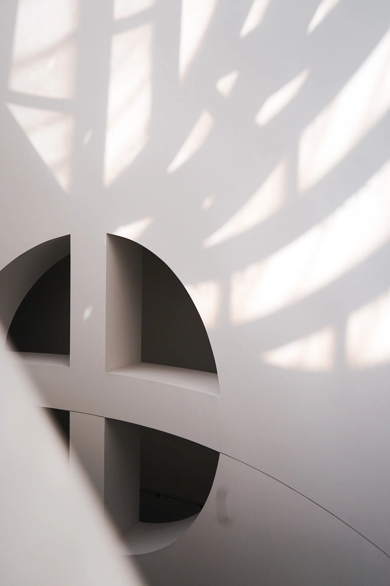 Abstract architectural interior with curved openings and shadows cast on the ceiling.