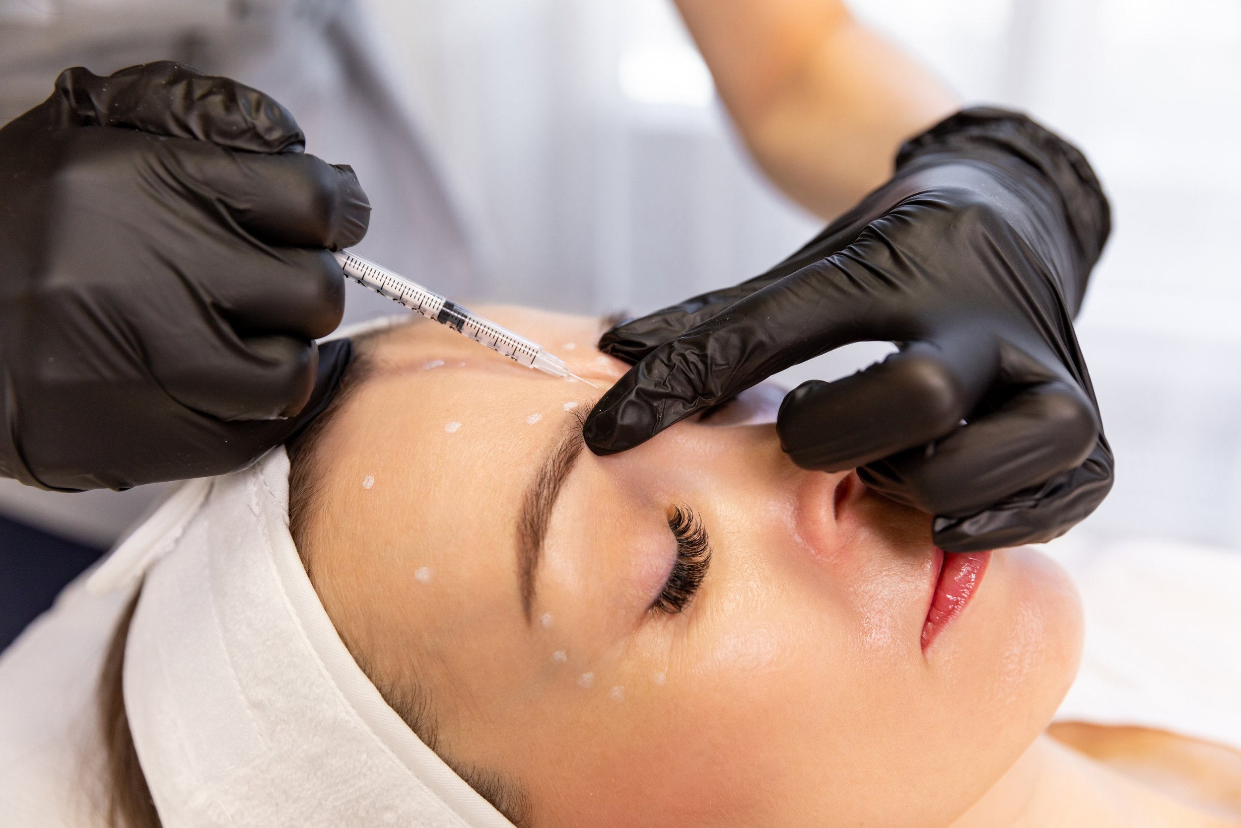 A woman receiving a cosmetic injection or Botox treatment on her forehead from a professional wearing black gloves.