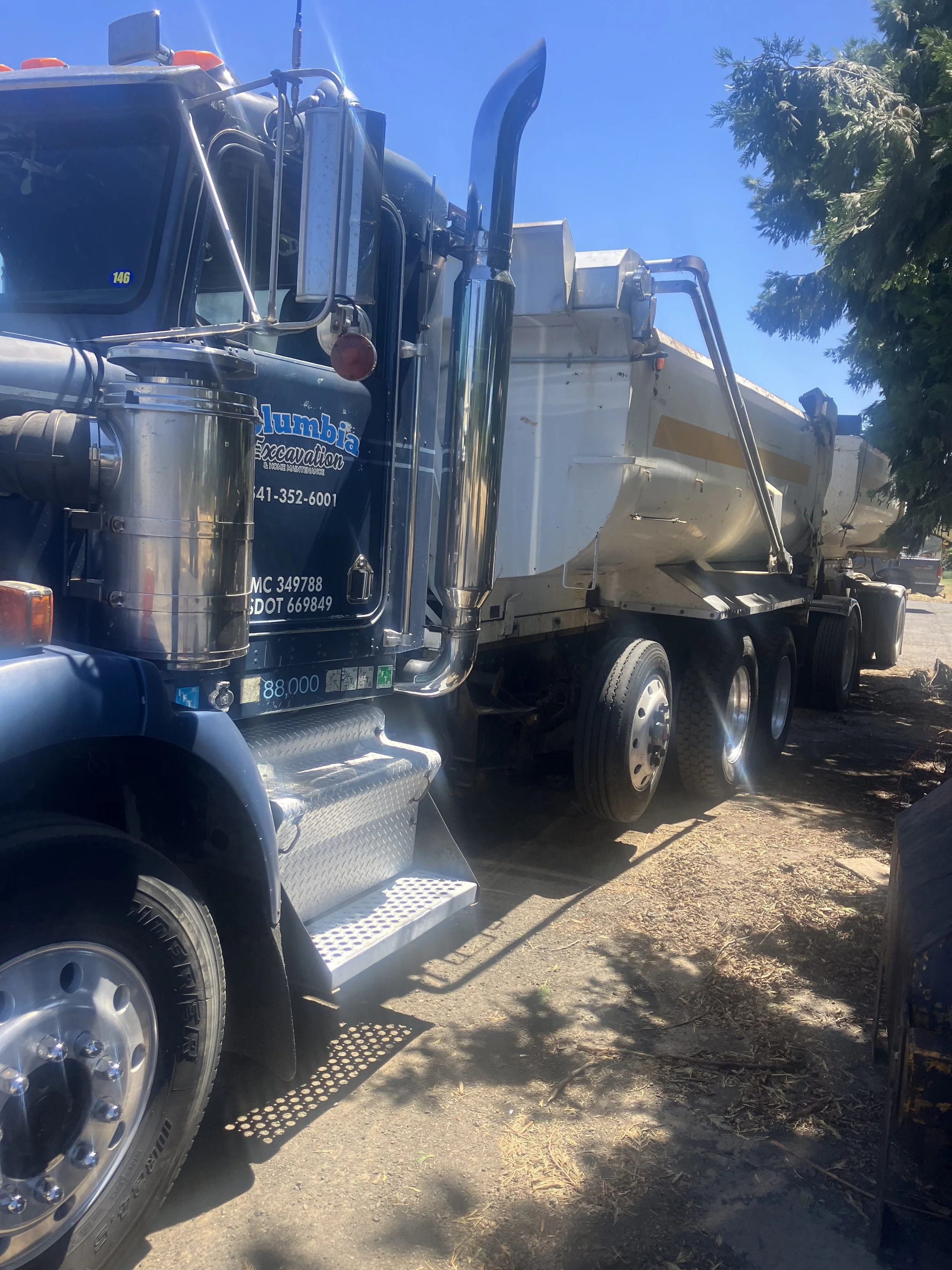 Close-up view of a large black and white dump truck parked outdoors on a sunny day, with trees in the background.