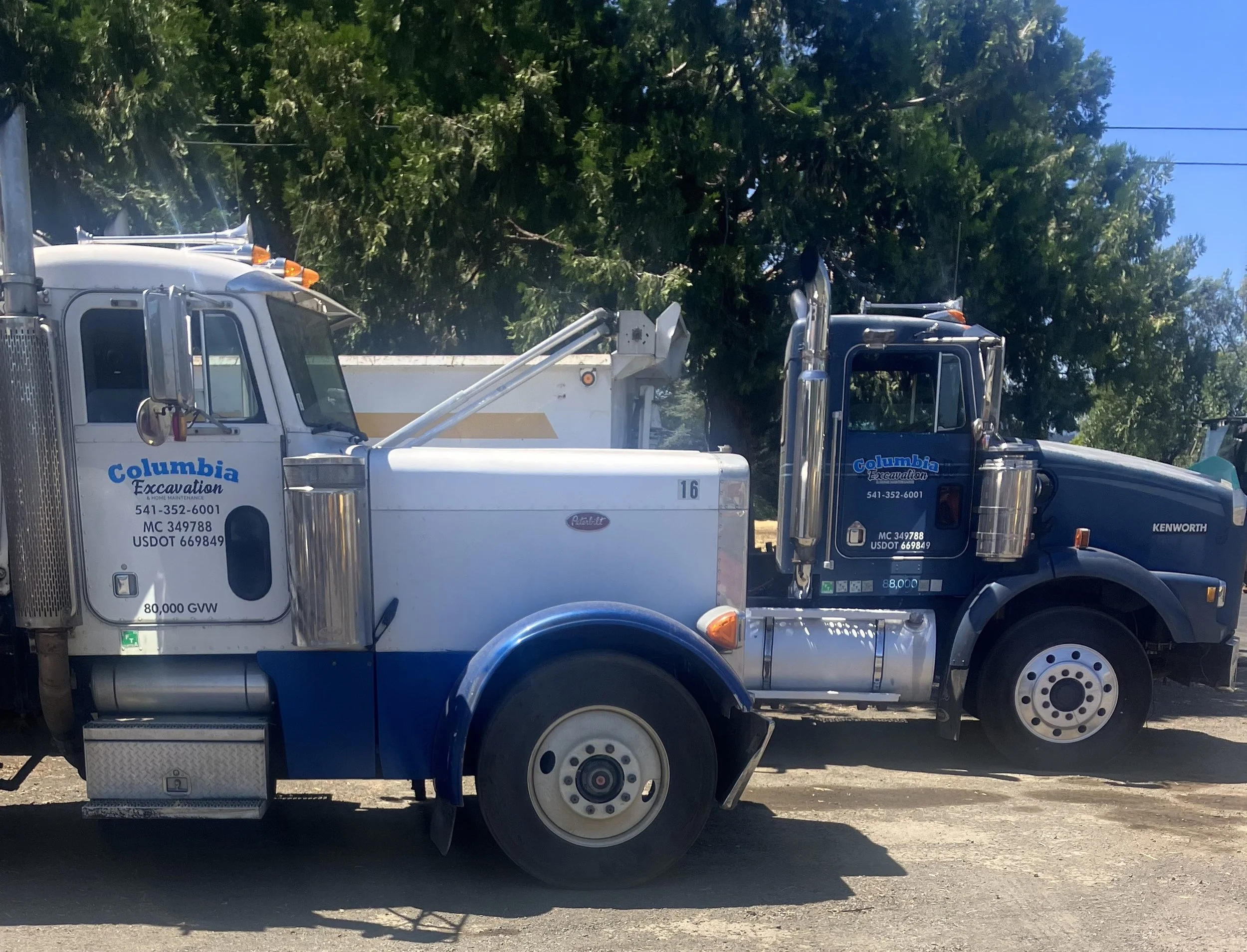 A large white and blue Columbia Excavation truck parked outdoors, with trees and a clear blue sky in the background.