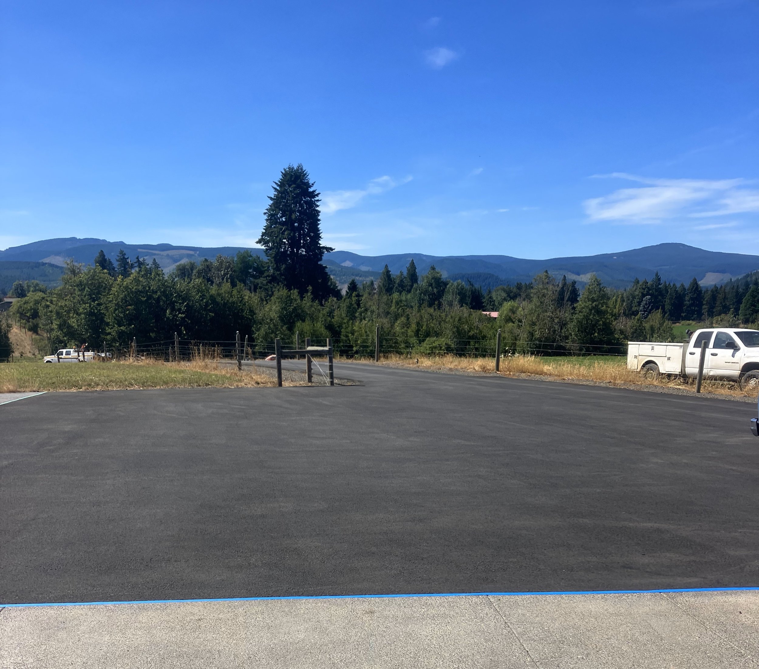 Empty parking lot with rolling hills and trees in the background, blue sky with some clouds.