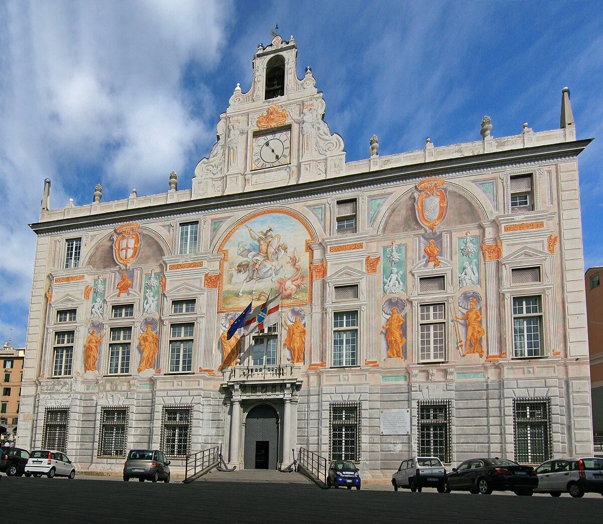 The Bank of Saint George (Casa di san Giorgio) in Genoa is shown as a fortified medieval stone building near the port, with large windows and historic painted frescoes. It is often described as the world's first modern bank.