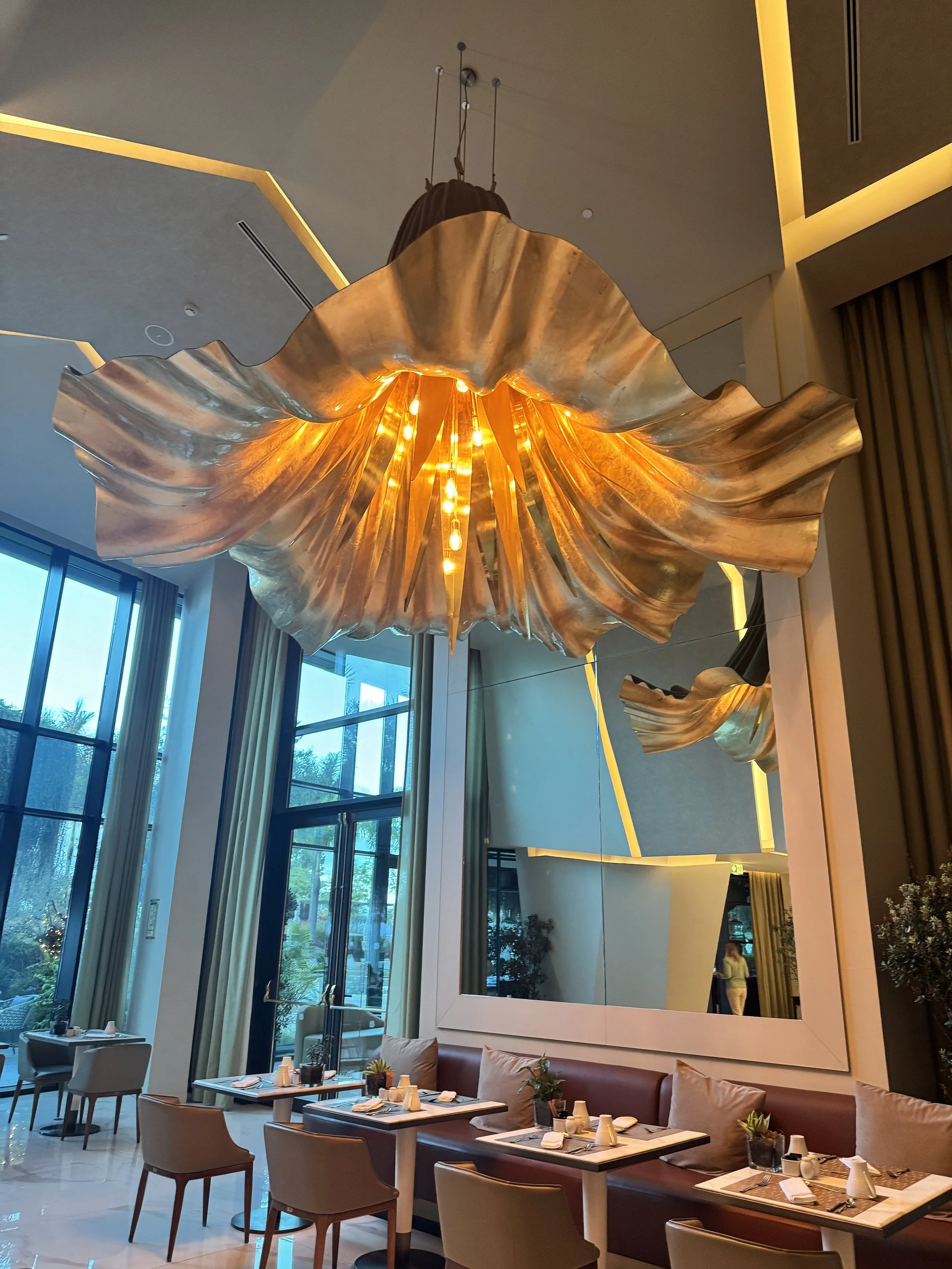 An elegant, oversized flower-shaped light fixture blooms above the breakfast room at Savoy Palace, its layered petals softly glowing and cascading overhead.