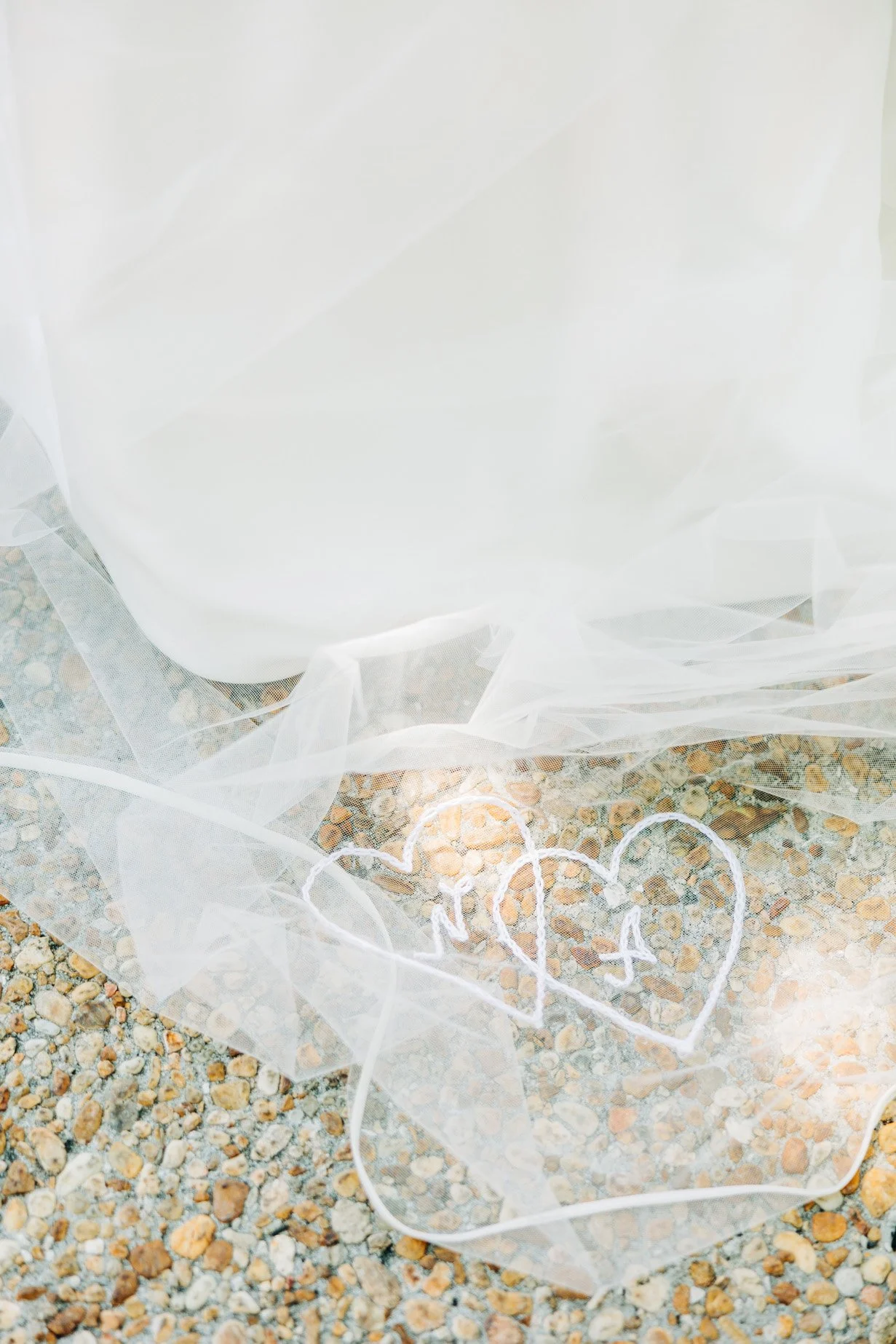 Two hearts drawn with white chalk on a gravel surface, partially covered by a sheer white fabric.