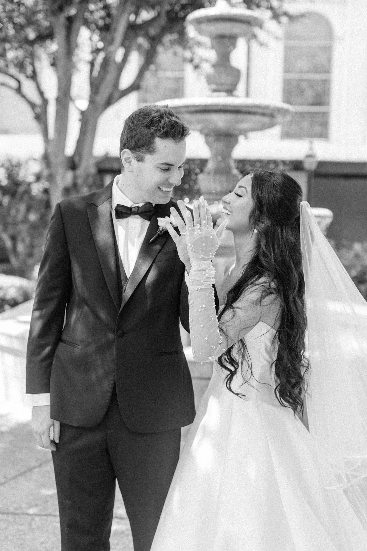 A bride and groom sharing a joyful moment outside during their wedding, with the bride playfully touching the groom's face.