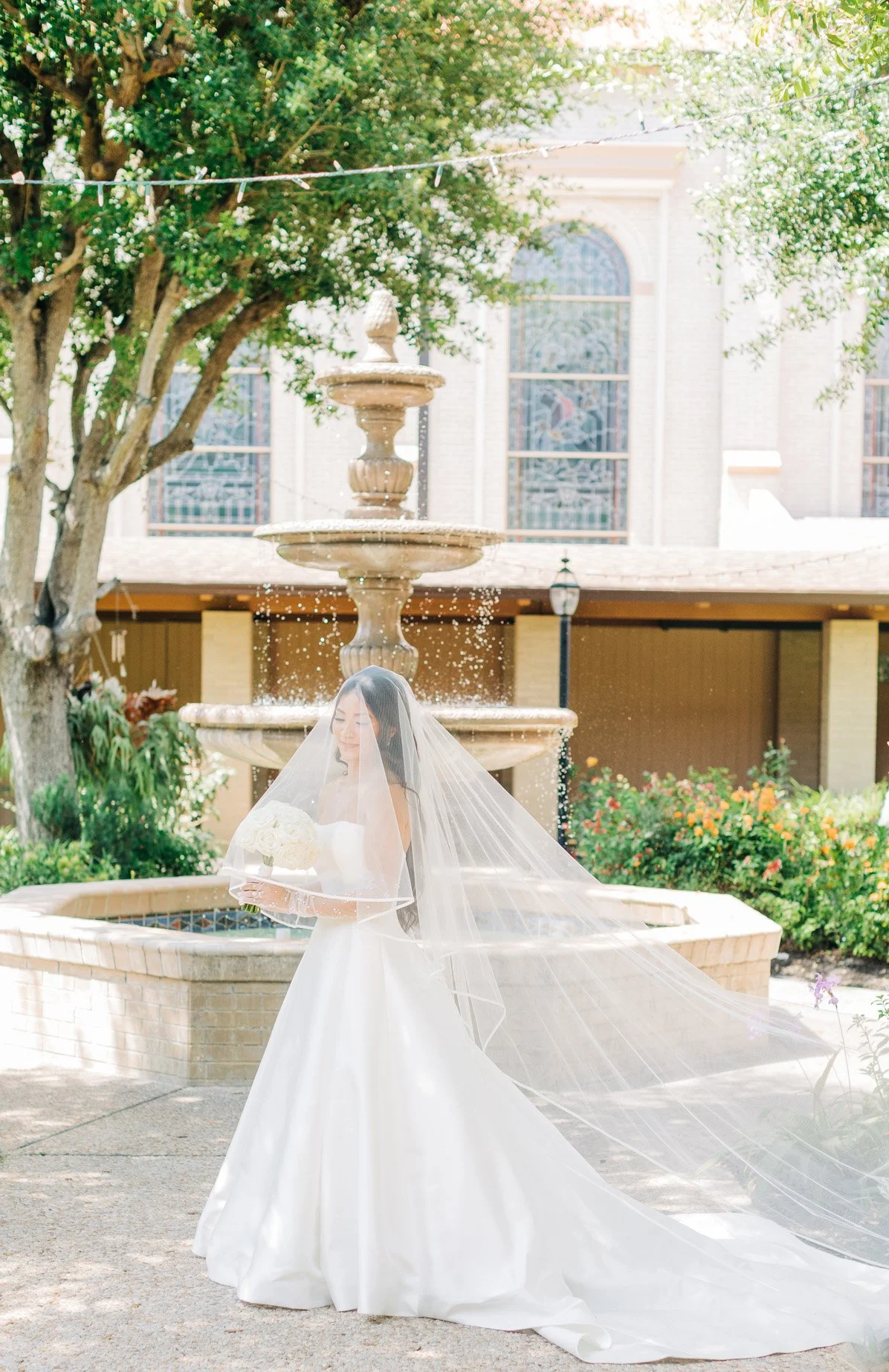Bridal bride standing outdoors near a fountain holding a bouquet of white roses