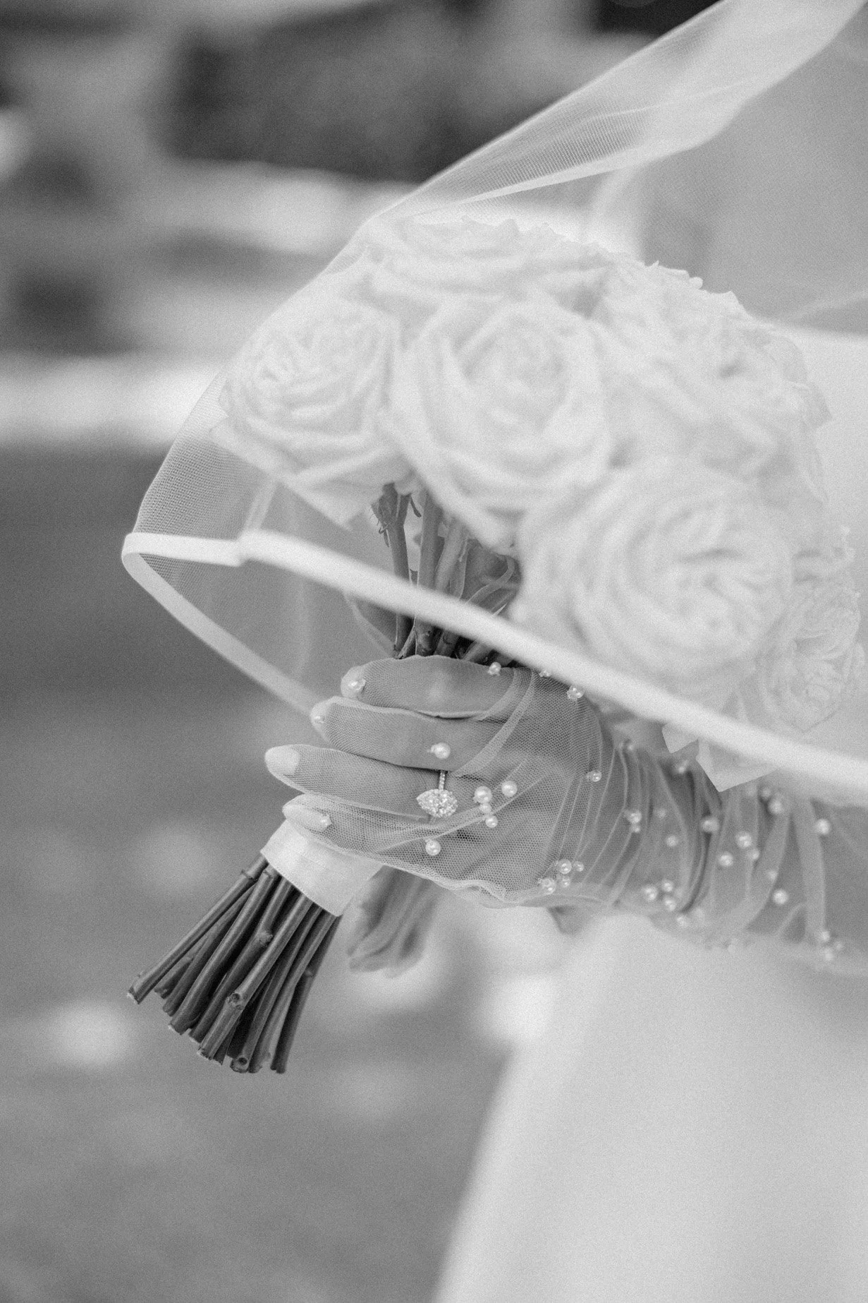 A hand holding a bouquet of roses wrapped in tulle fabric.