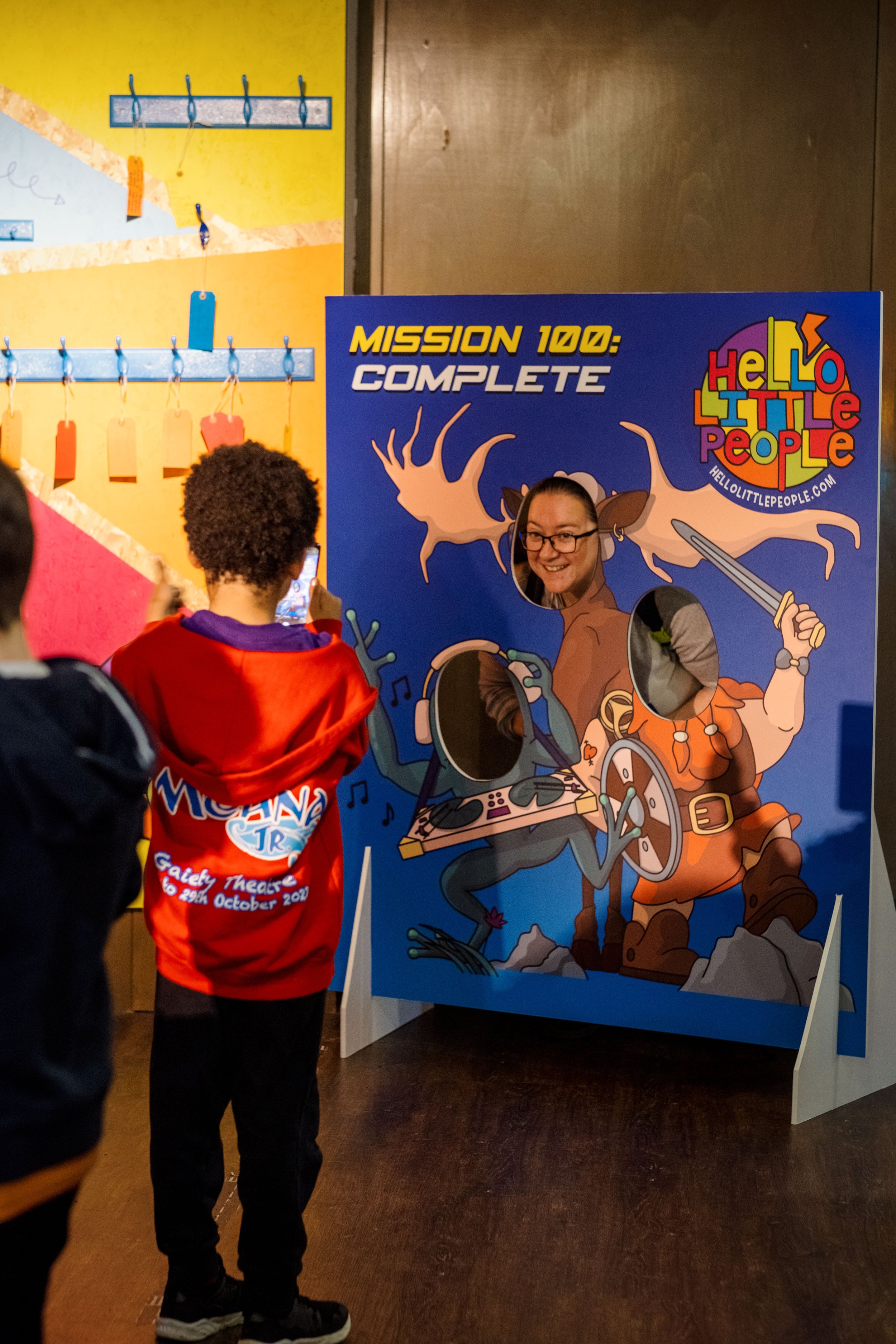 Child taking photo of person using a face cutout board with cartoon characters at an event.