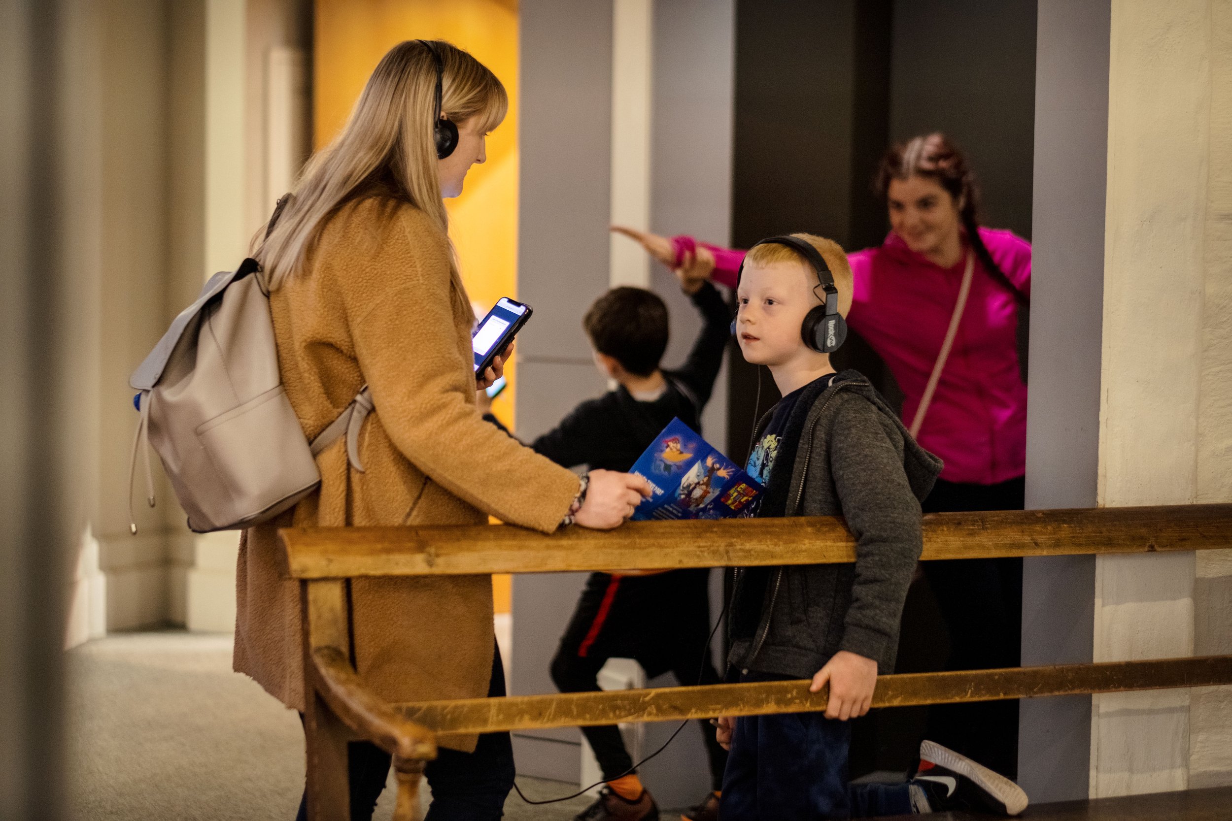 People wearing headphones in a museum, woman with phone and boy with brochure