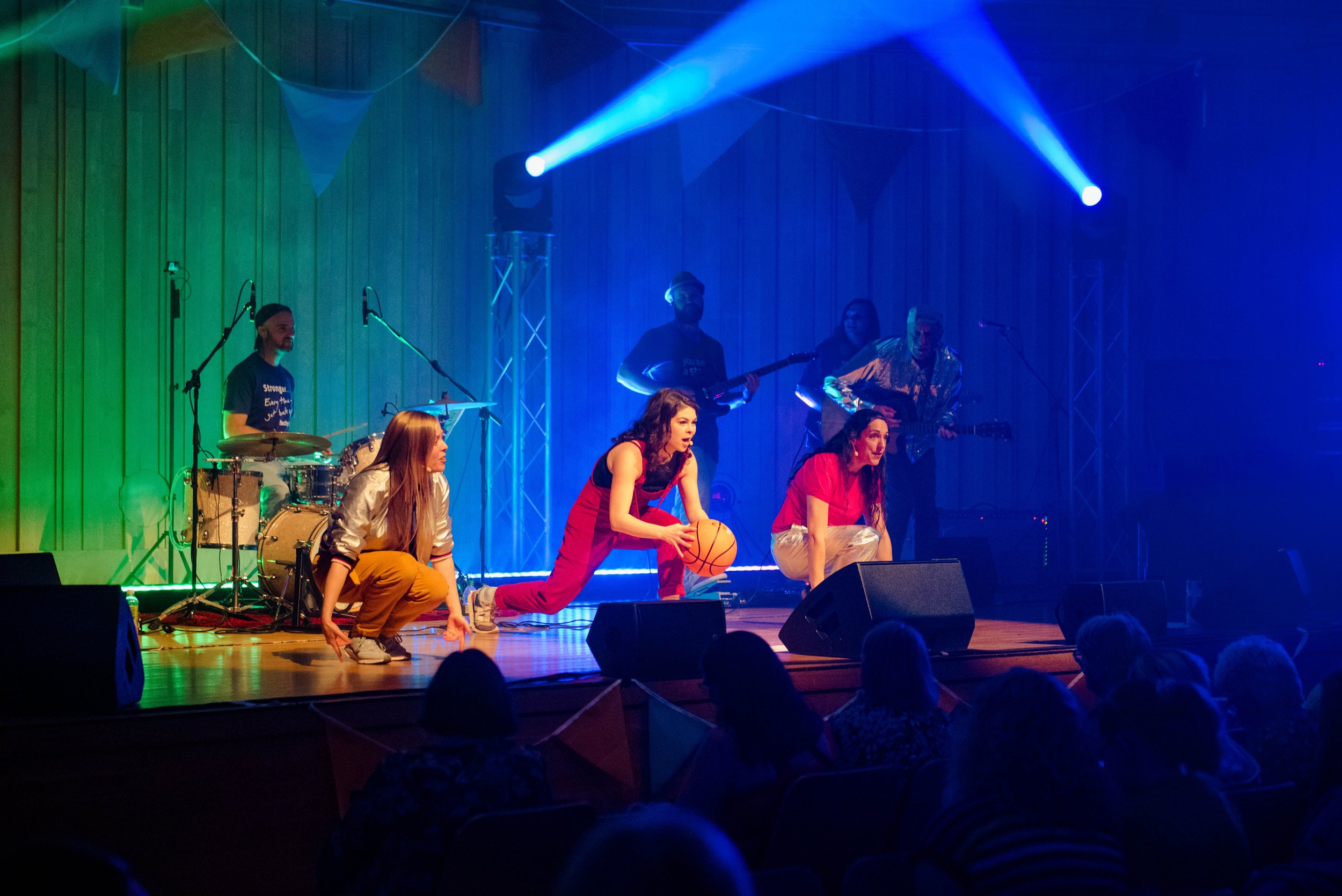 Live performance on stage with people dancing and playing musical instruments under bright stage lights.