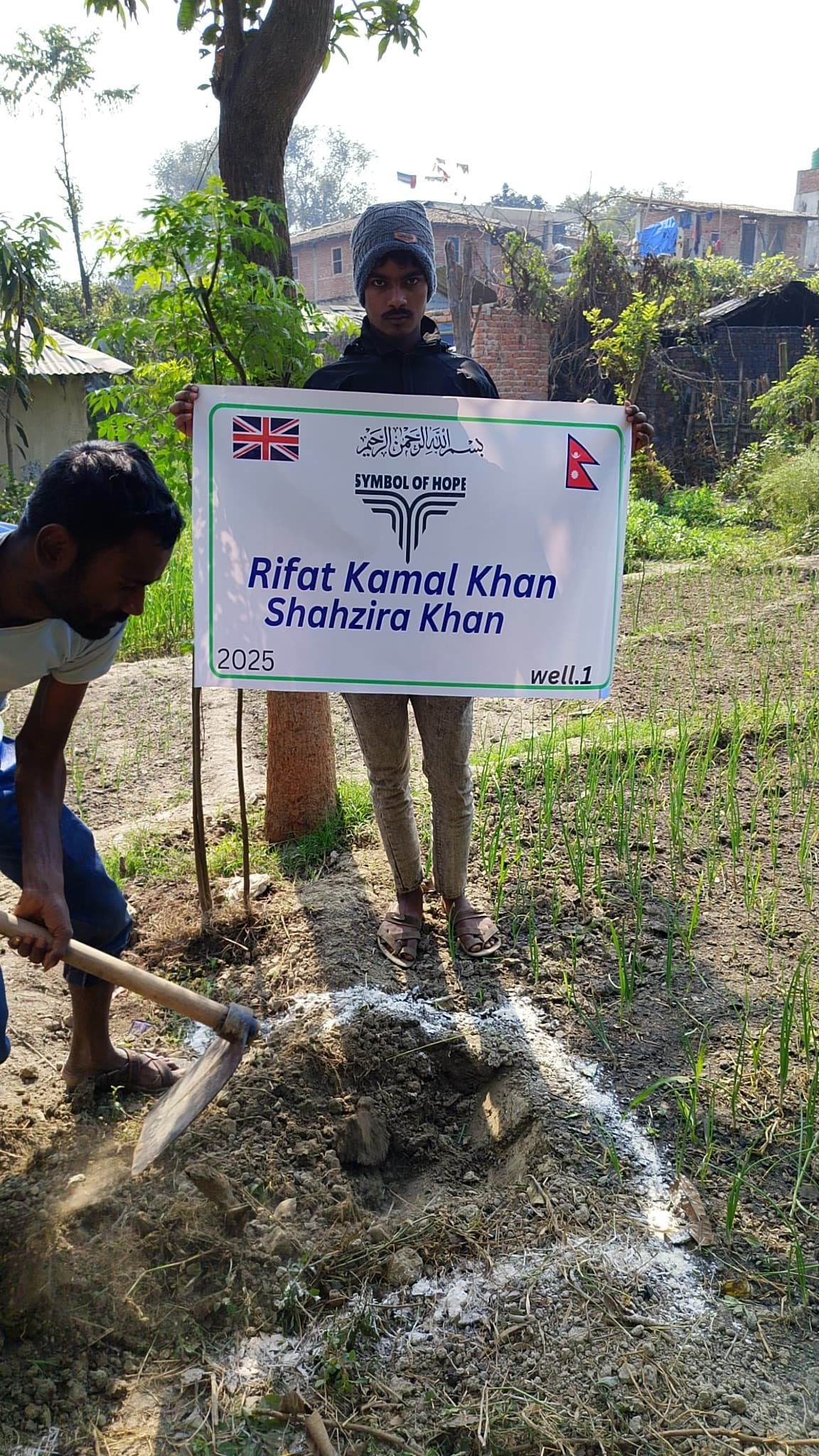 Two people in a rural setting, one holding a sign with text, another digging.