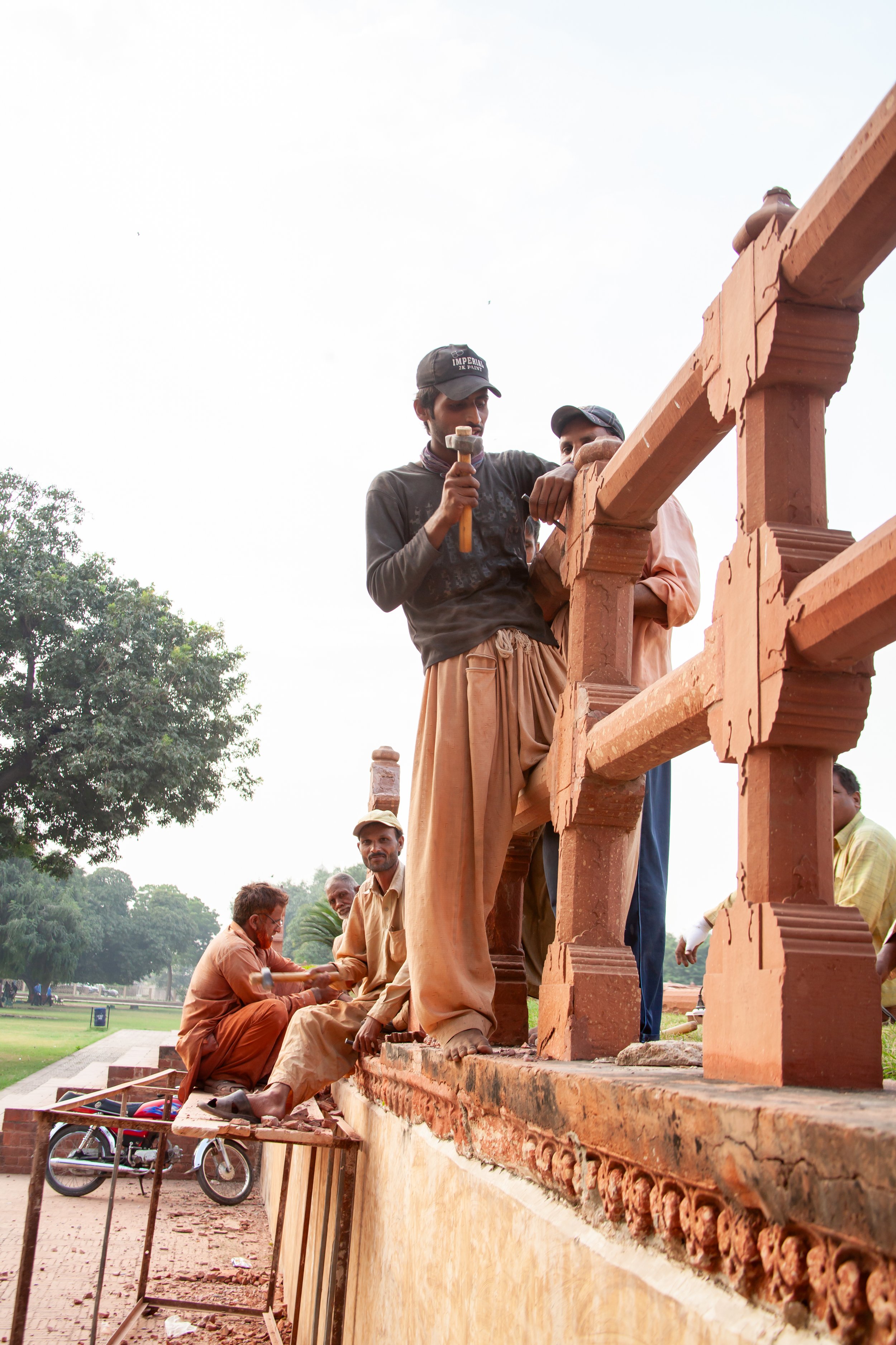Group of workers restoring a historic building with red stone and detailing outdoors.
