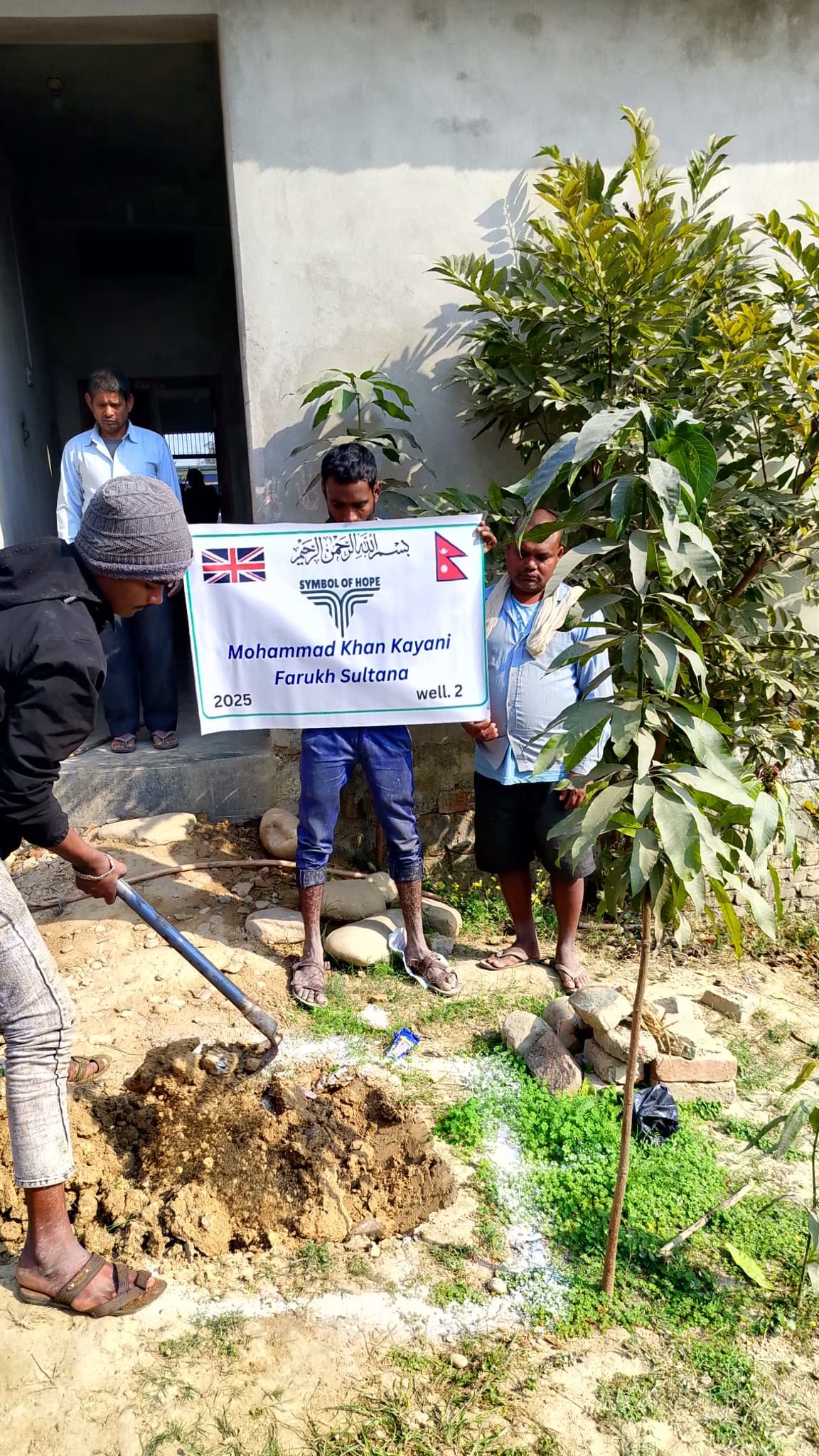 People planting a tree with a banner that reads 'Symbol of Hope' and flags of the UK and Nepal.
