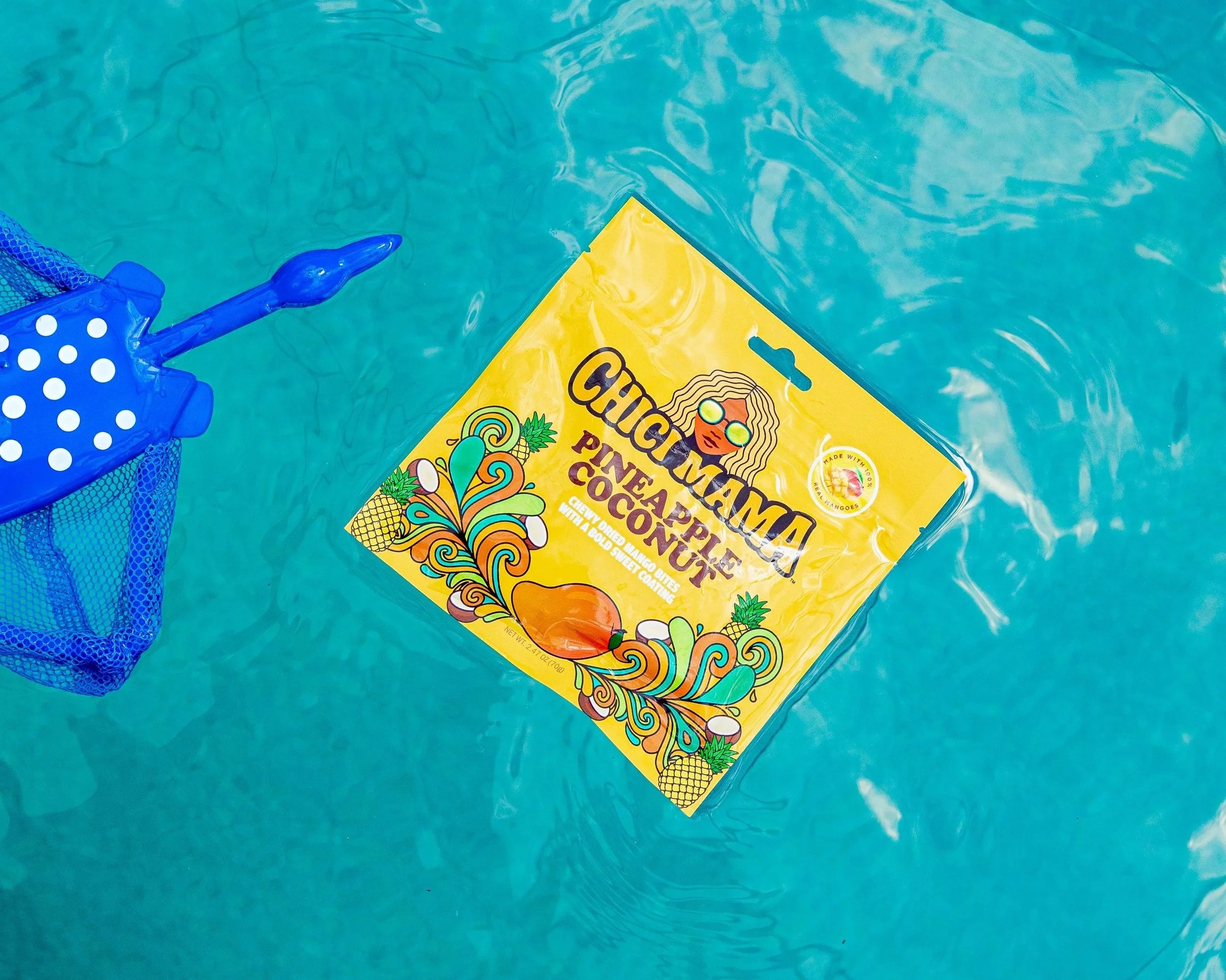 Chici Mama Pineapple Coconut bag floating in pool next to blue beach toy, playful product photography by Gabe Gonzalez