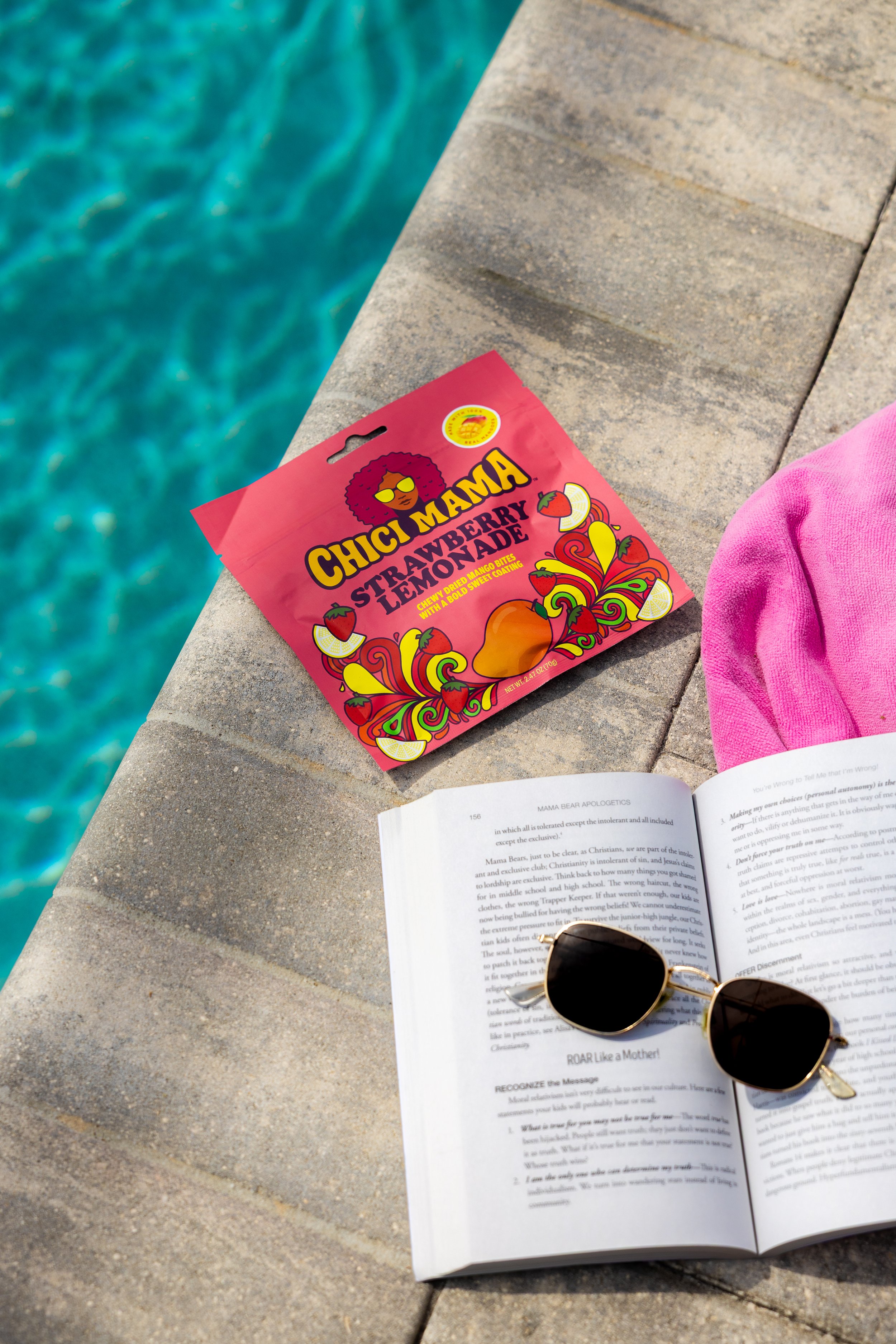 Overhead flat lay of Chici Mama snack bag on yellow striped beach towel with sunscreen and pool accessories
