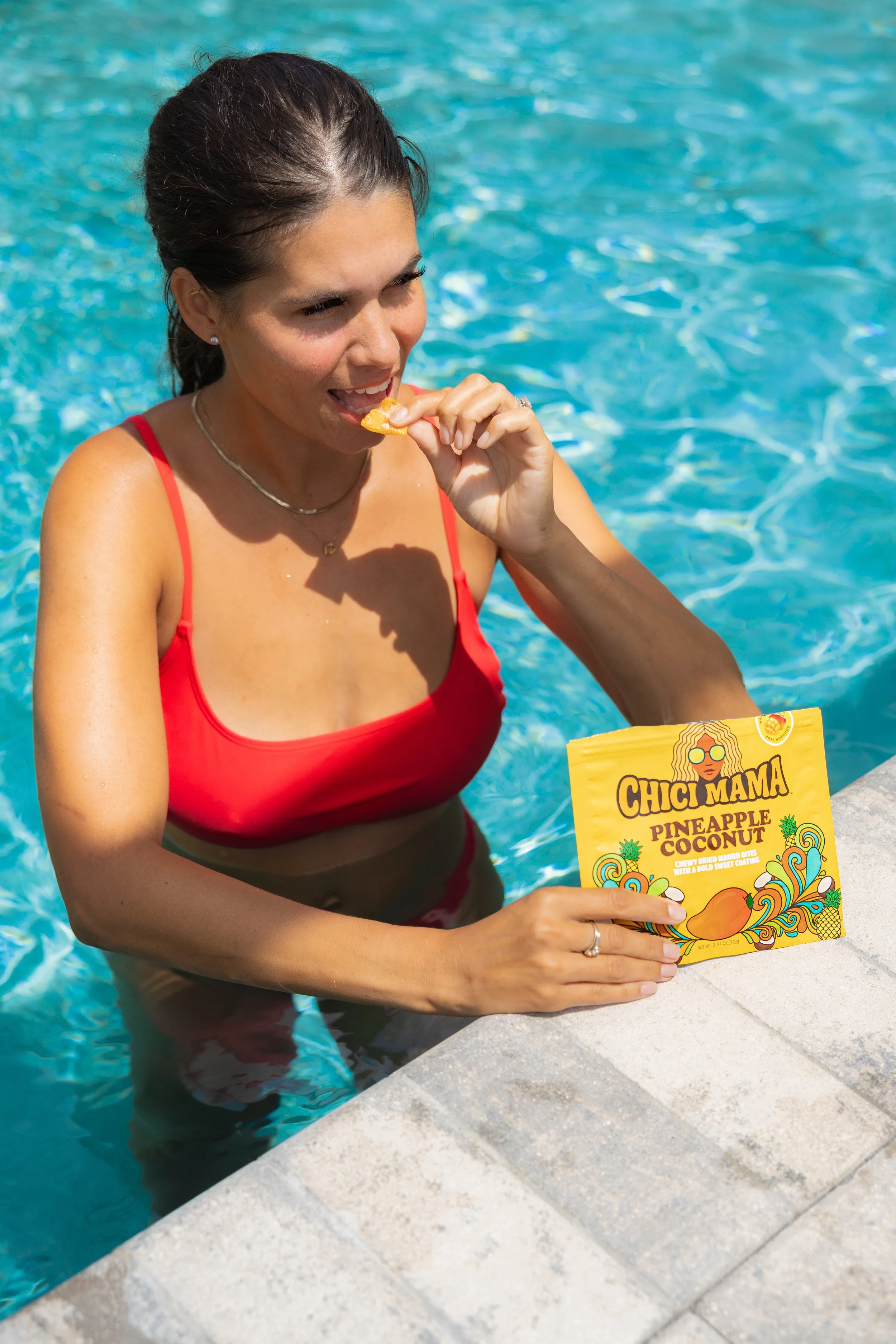 Woman in red swimsuit eating Chici Mama snack in pool, summer lifestyle content creation by Gabe Gonzalez